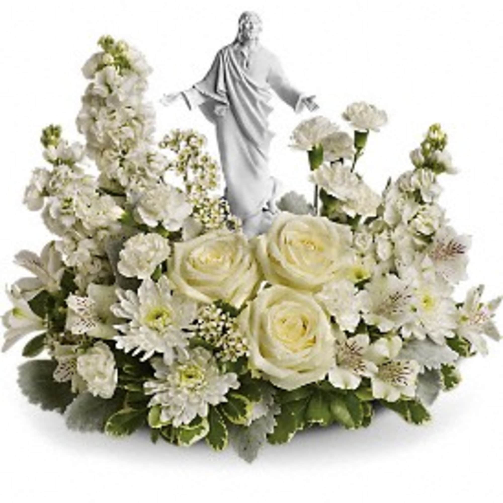 White floral arrangement with roses and carnations surrounding a white religious figurine.