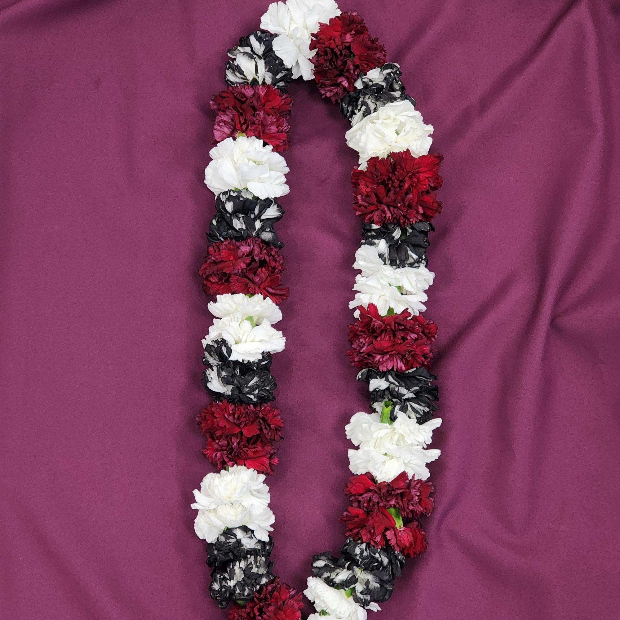 Lei-style garland of red, white, and black carnations arranged in a loop on a purple cloth.