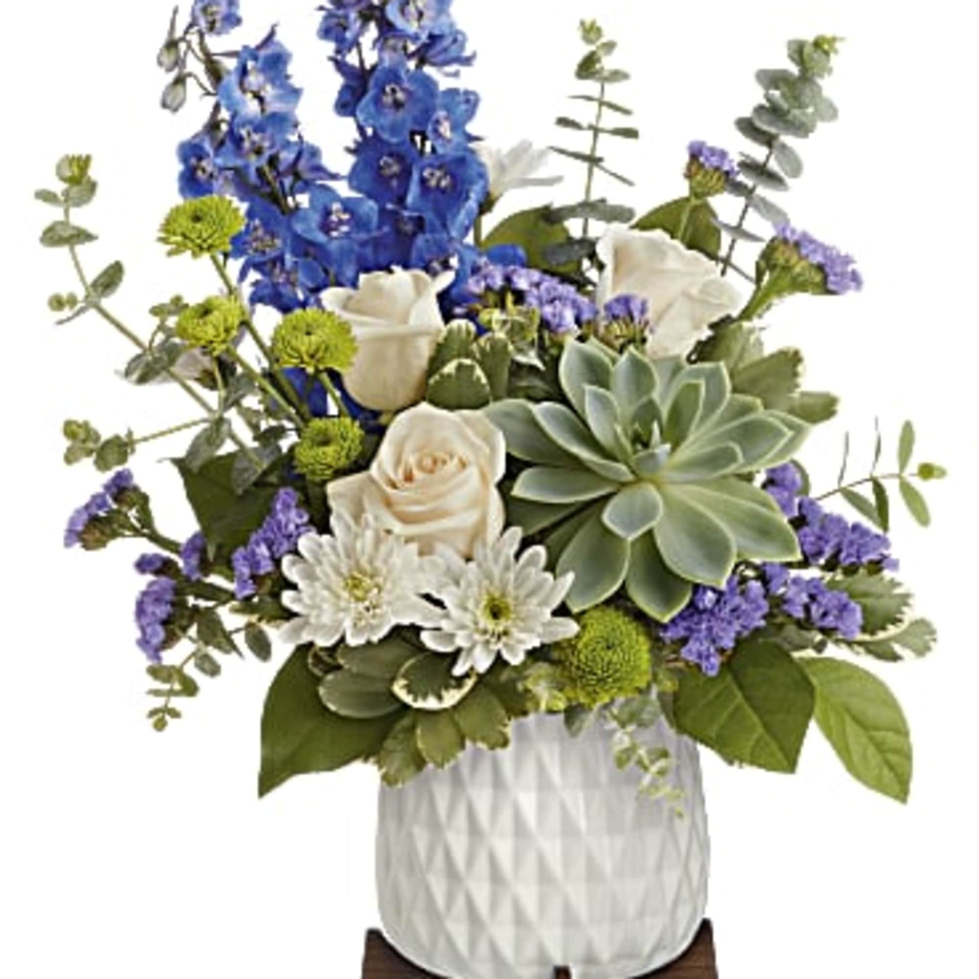 Arrangement with blue delphinium, white roses, succulents and mums in a white pot on a wooden stand