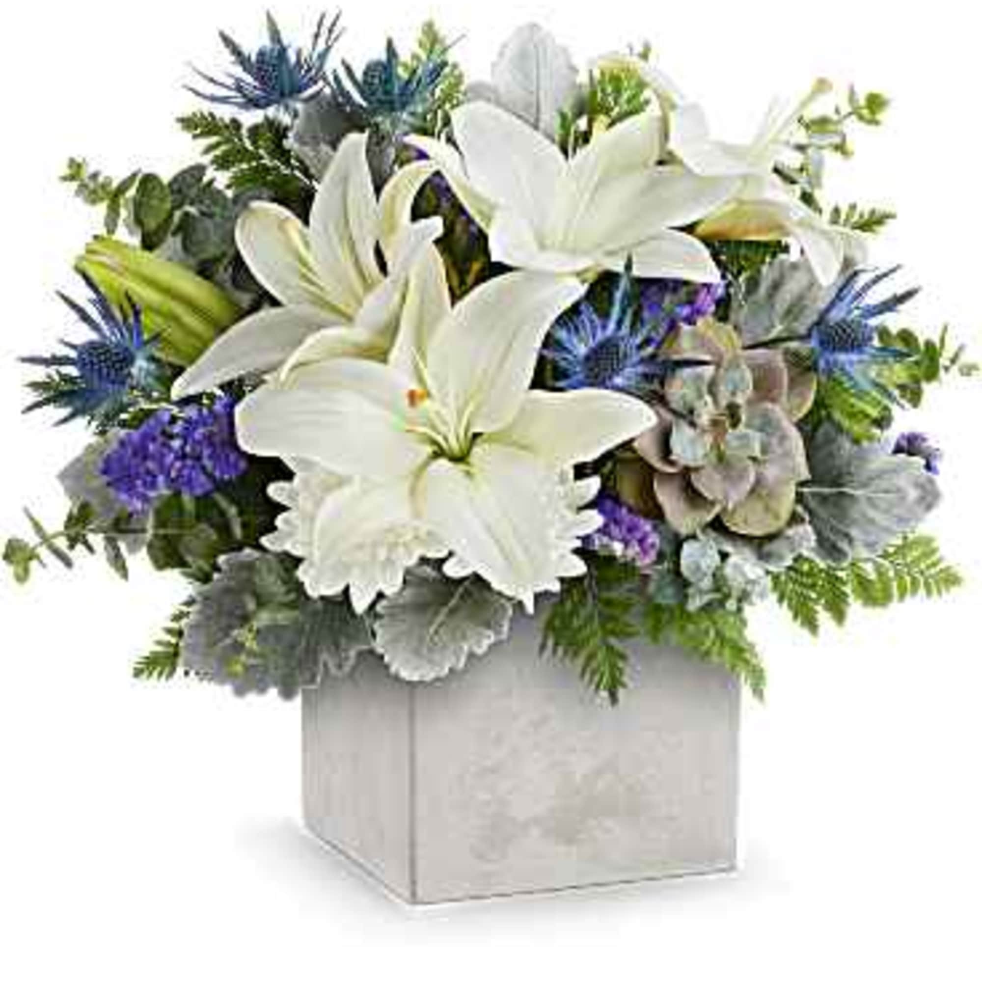 Low arrangement of white lilies, blue flowers, and a succulent in a square white vase