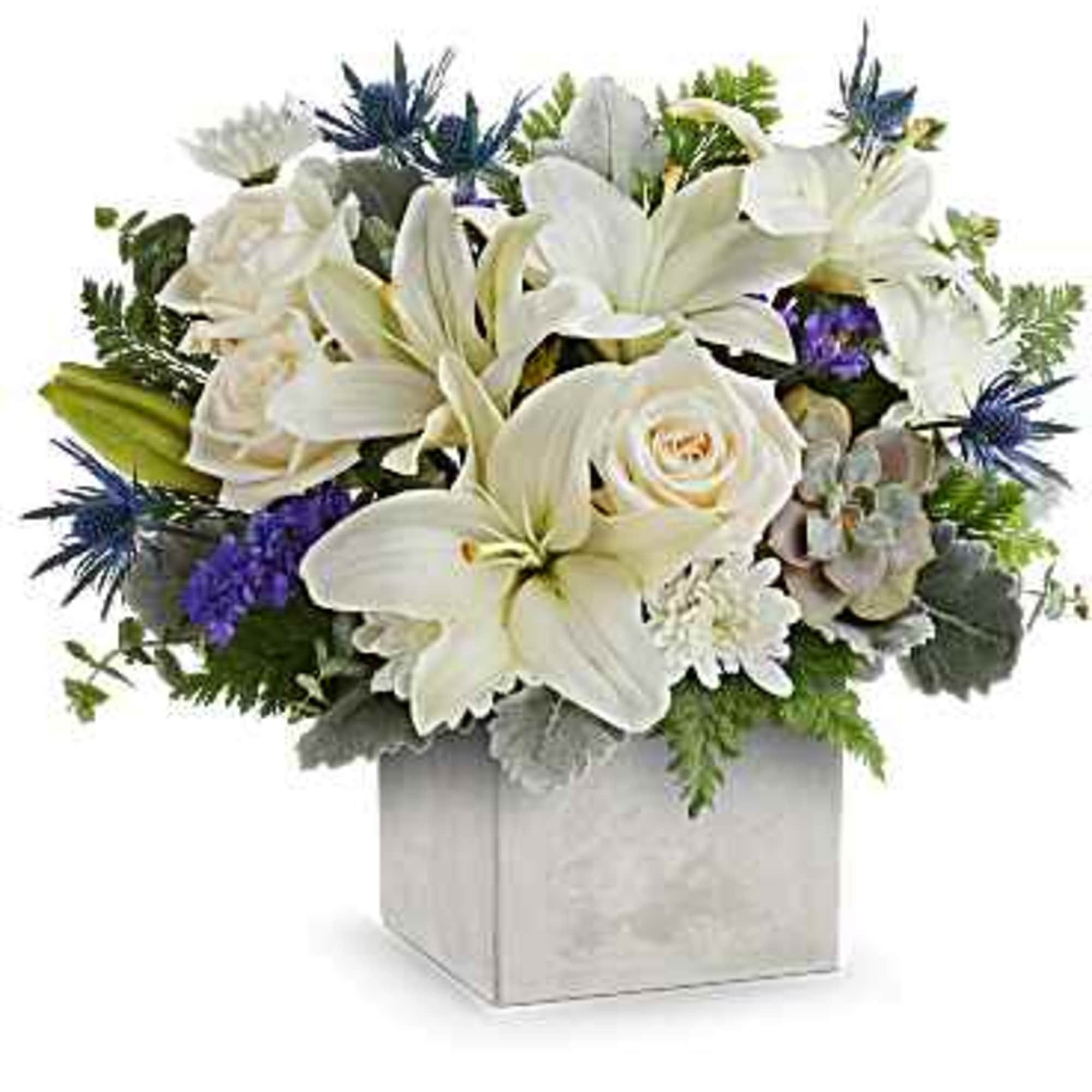 Low white lily and rose arrangement with blue accents in a square white cube vase