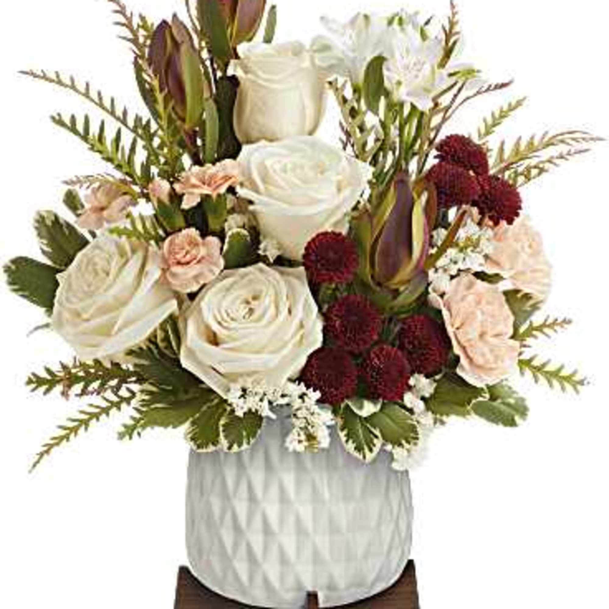 Arrangement of white roses, peach carnations, and burgundy mums in a white textured pot on a wooden stand.