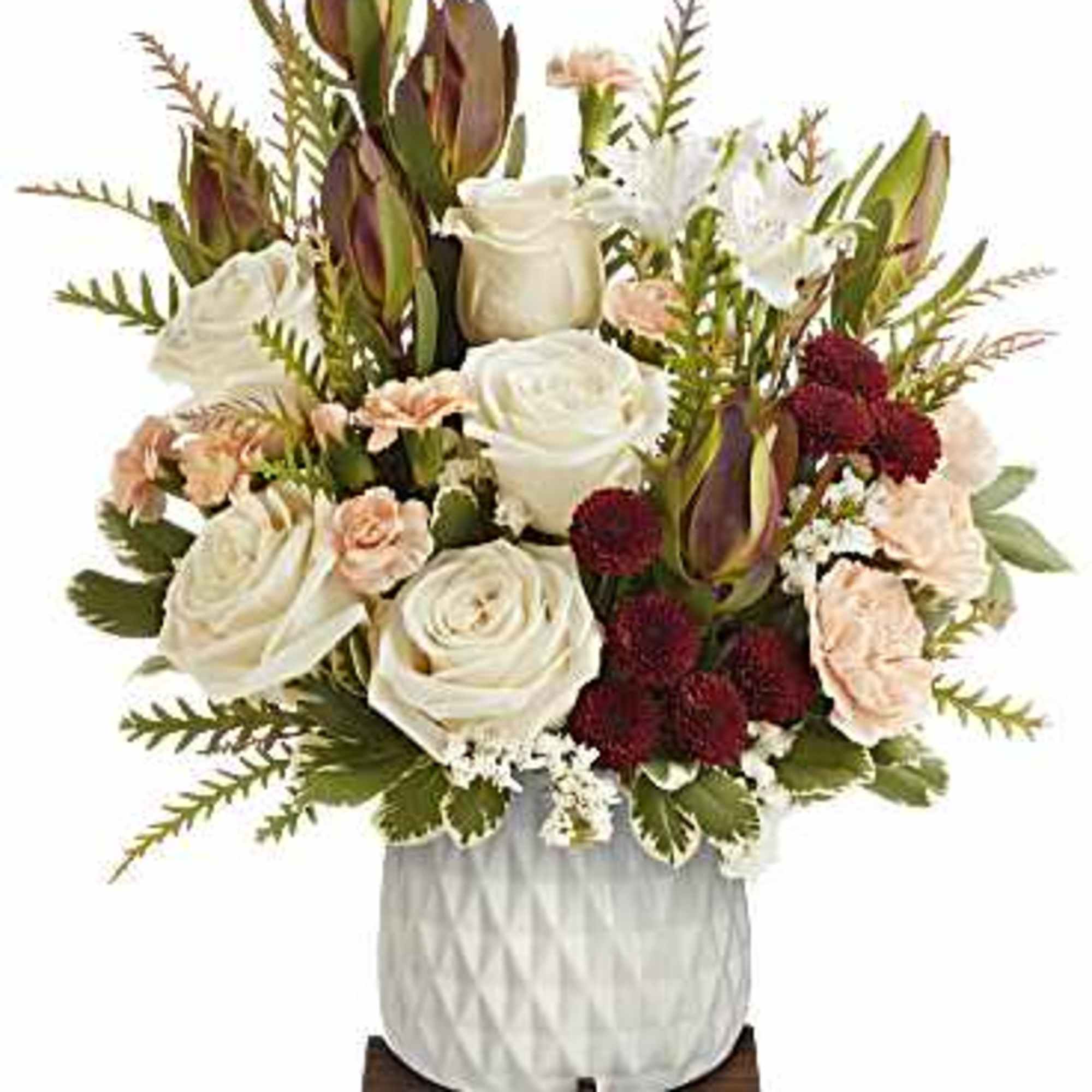 Arrangement of white roses, peach carnations and burgundy mums in a white ceramic pot on a wooden stand