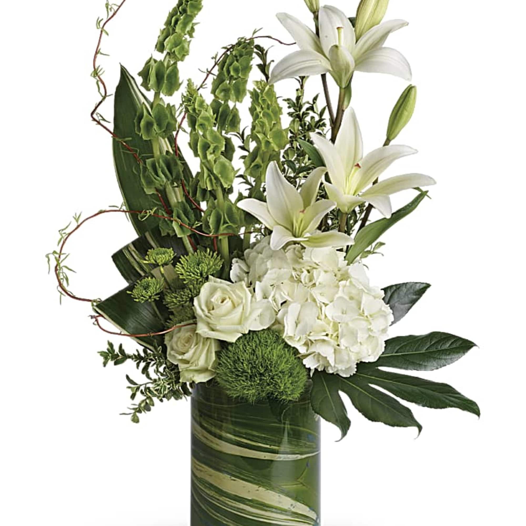 Tall arrangement of white lilies, roses, and hydrangeas with green accents in a clear glass cylinder vase