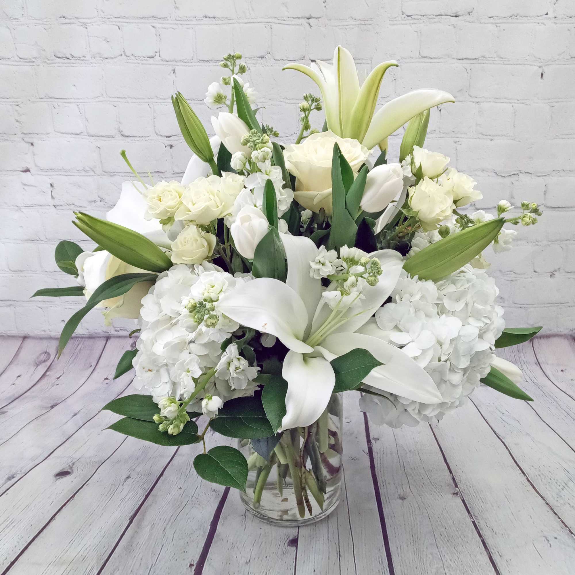 White lilies, roses, tulips, and hydrangeas arranged in a clear glass vase