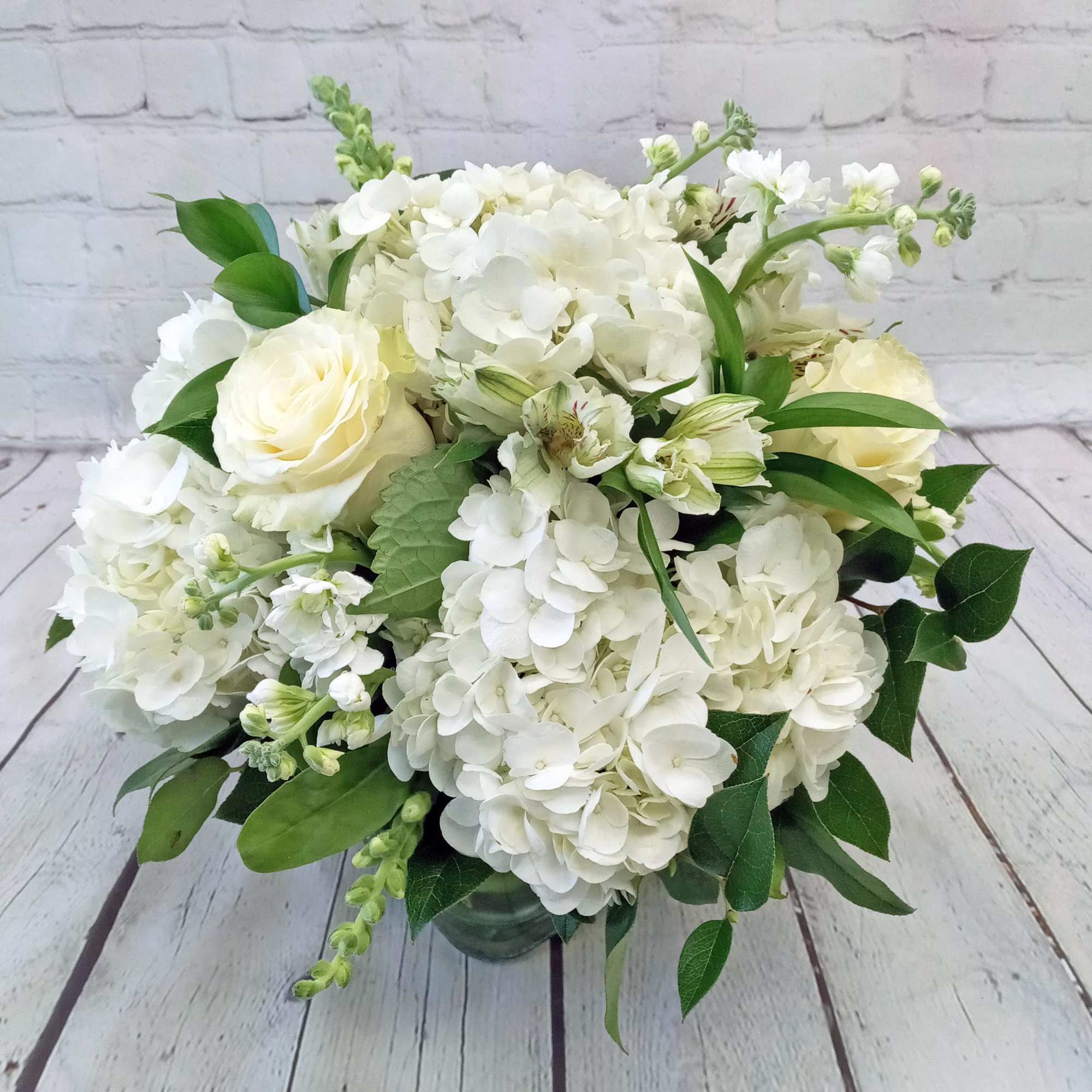 Round arrangement of white hydrangeas and cream roses in a clear glass vase