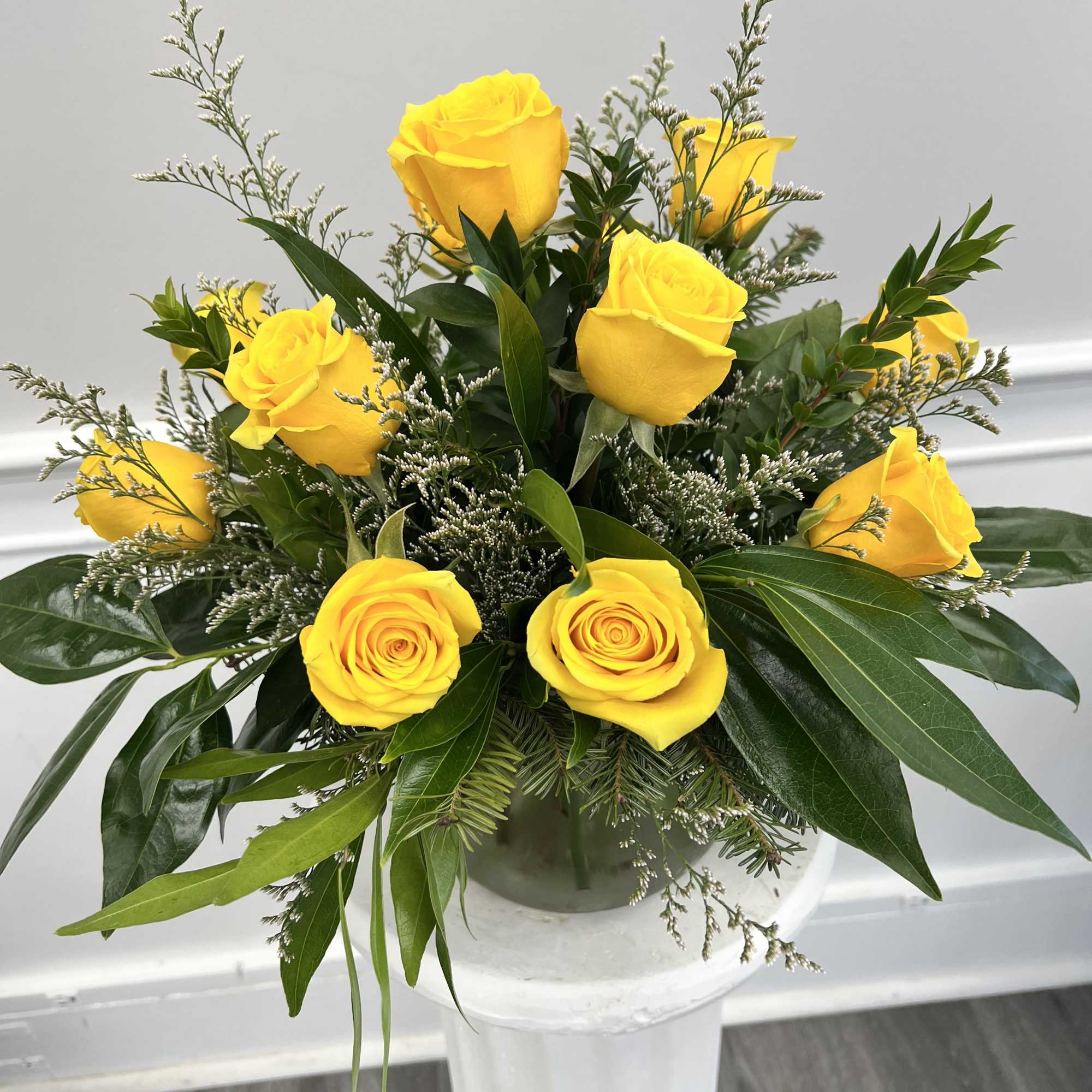 Arrangement of bright yellow roses with long green foliage in a glass vase.