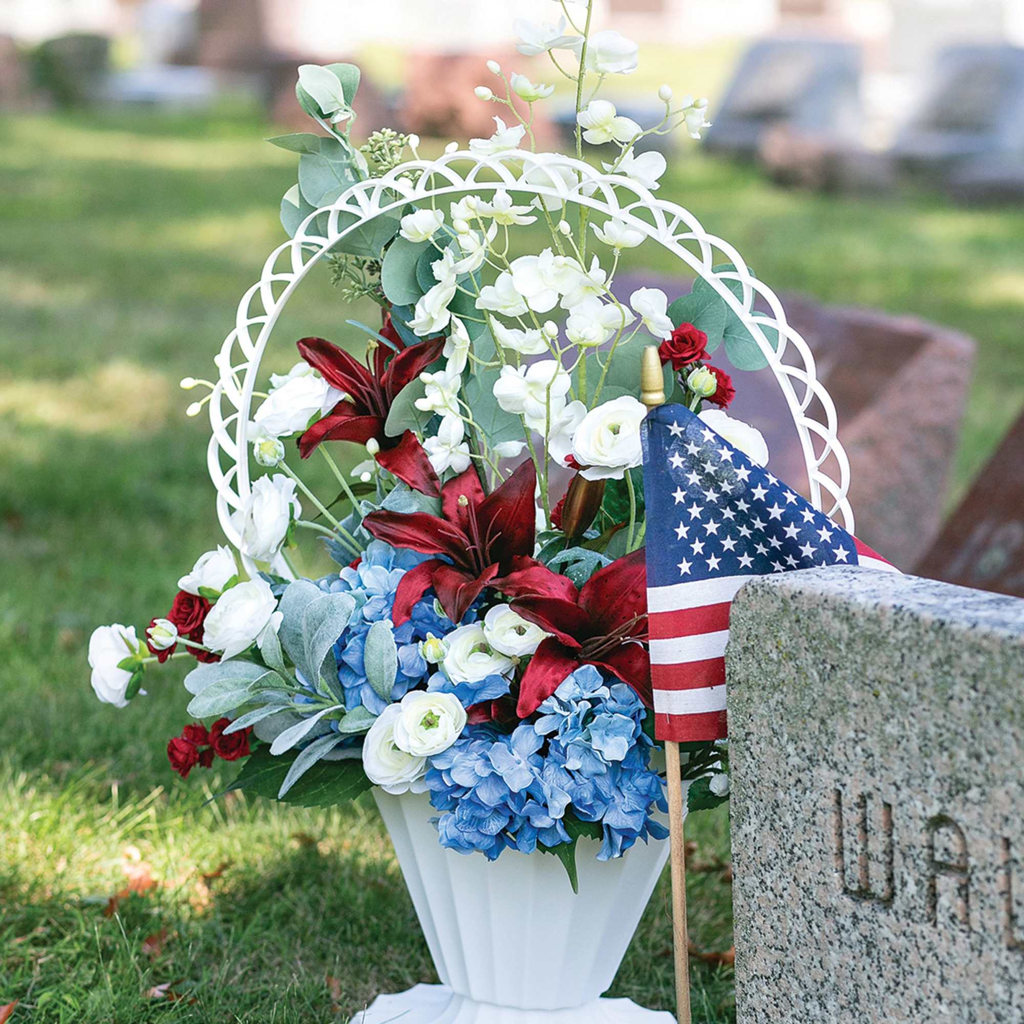 Memorial flower arrangement in a white urn with red, white, and blue flowers
