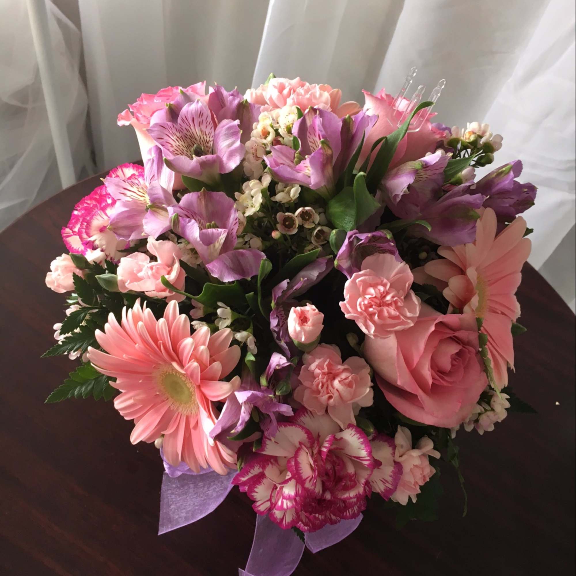 Compact bouquet of pink roses, gerbera daisies, carnations and lavender alstroemeria with a purple ribbon.