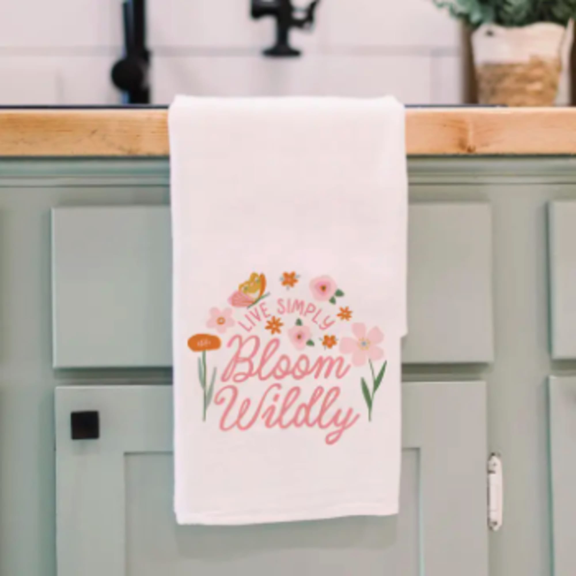 White towel with pink floral "Bloom Wildly" text