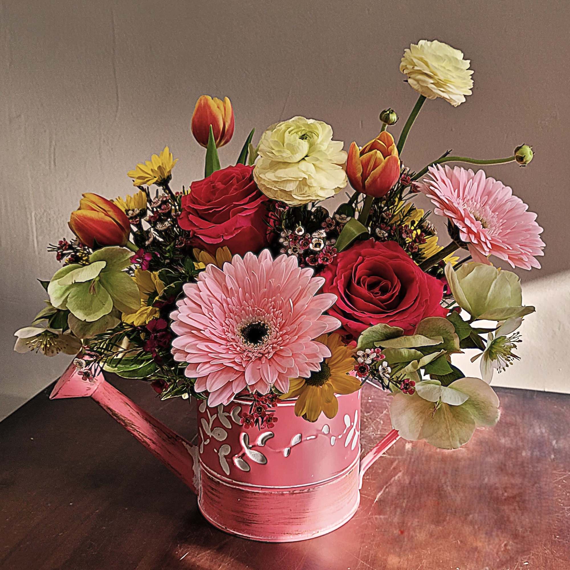 A colorful hammered watering can with an assortment of seasonal blossoms with