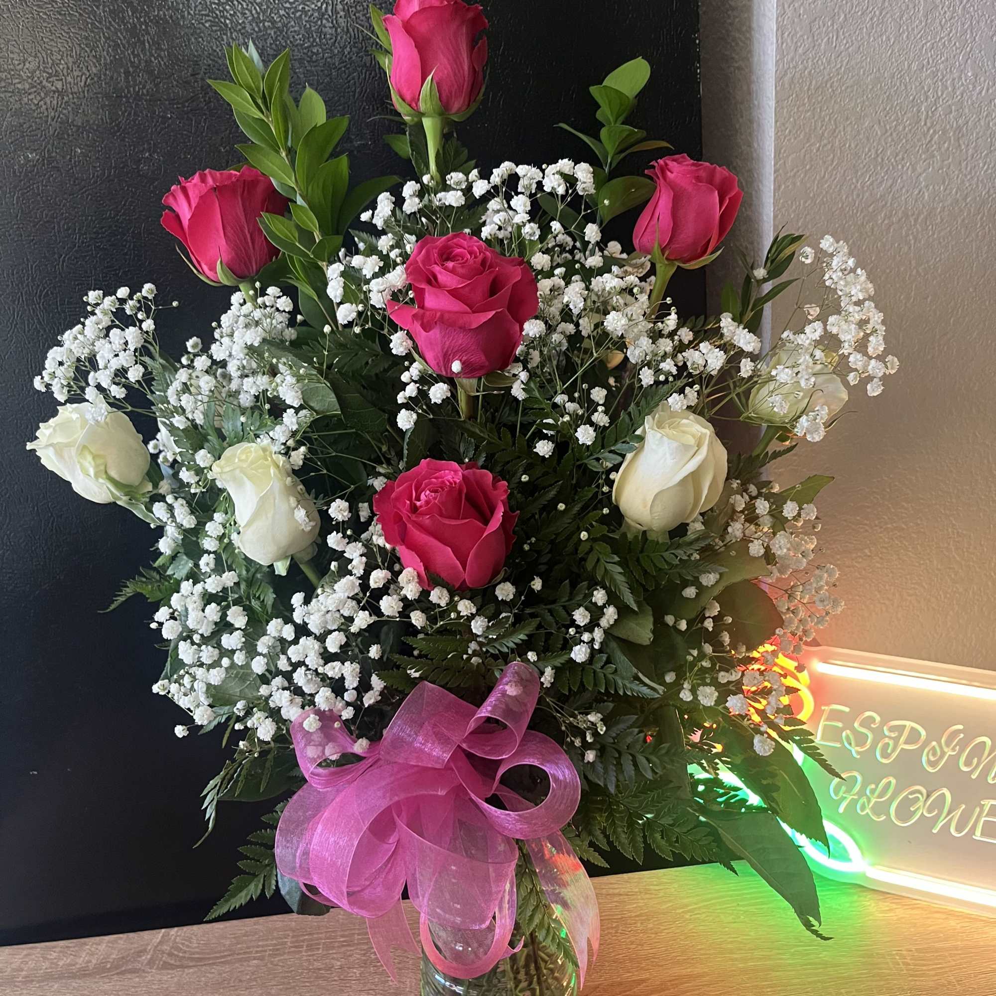 Tall vase arrangement of hot pink and white roses with baby's breath and a pink bow in a clear glass vase