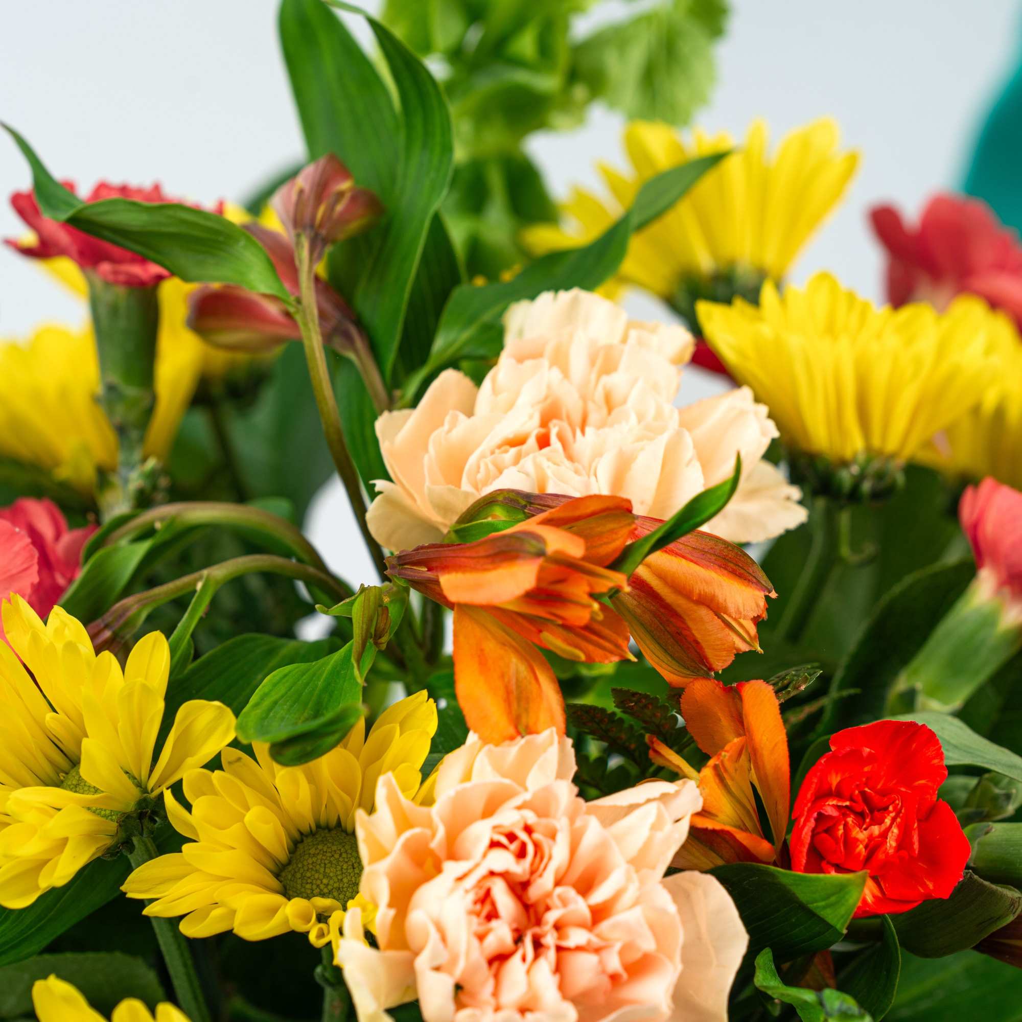 Bright mixed bouquet of peach carnations, yellow daisies, and orange blooms