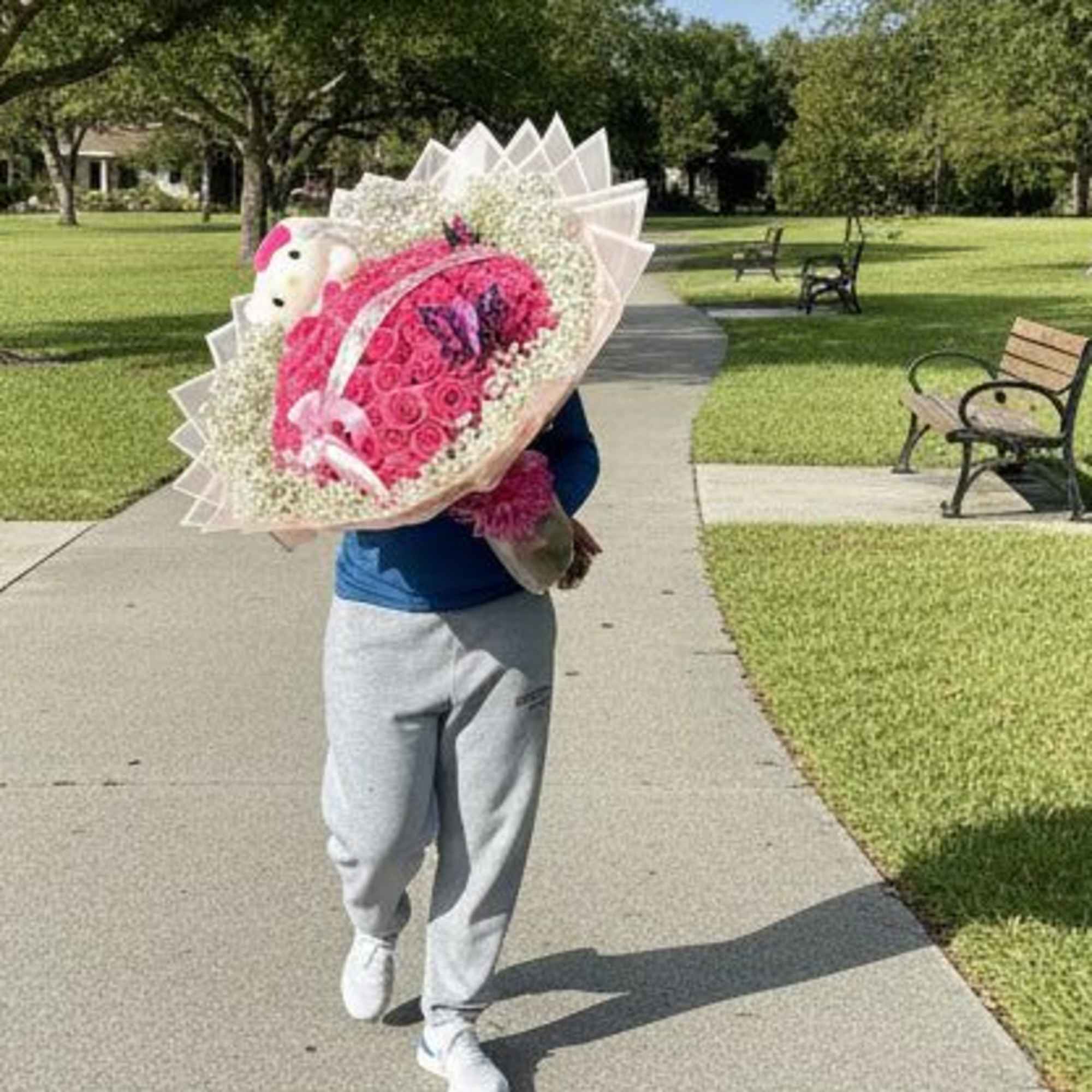 Large pink rose bouquet with a white teddy bear and ribbons carried along a park pathway