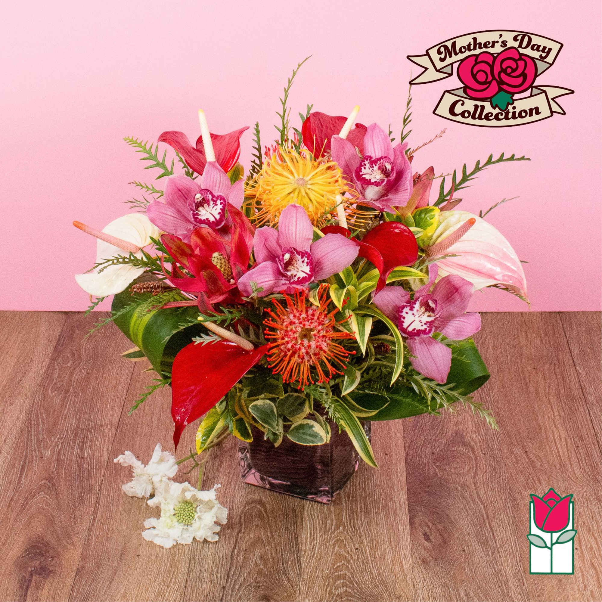 Tropical arrangement with pink orchids, red and white anthuriums, and orange protea in a dark glass cube vase.