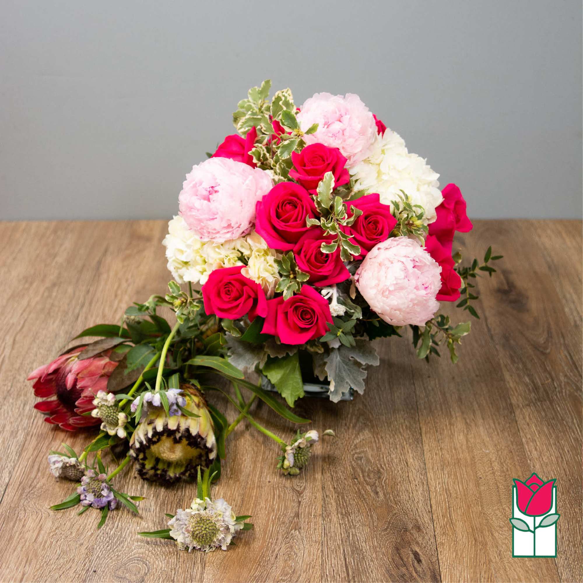 Compact arrangement of hot pink roses, pale pink peonies, and white blooms in a low glass vase.