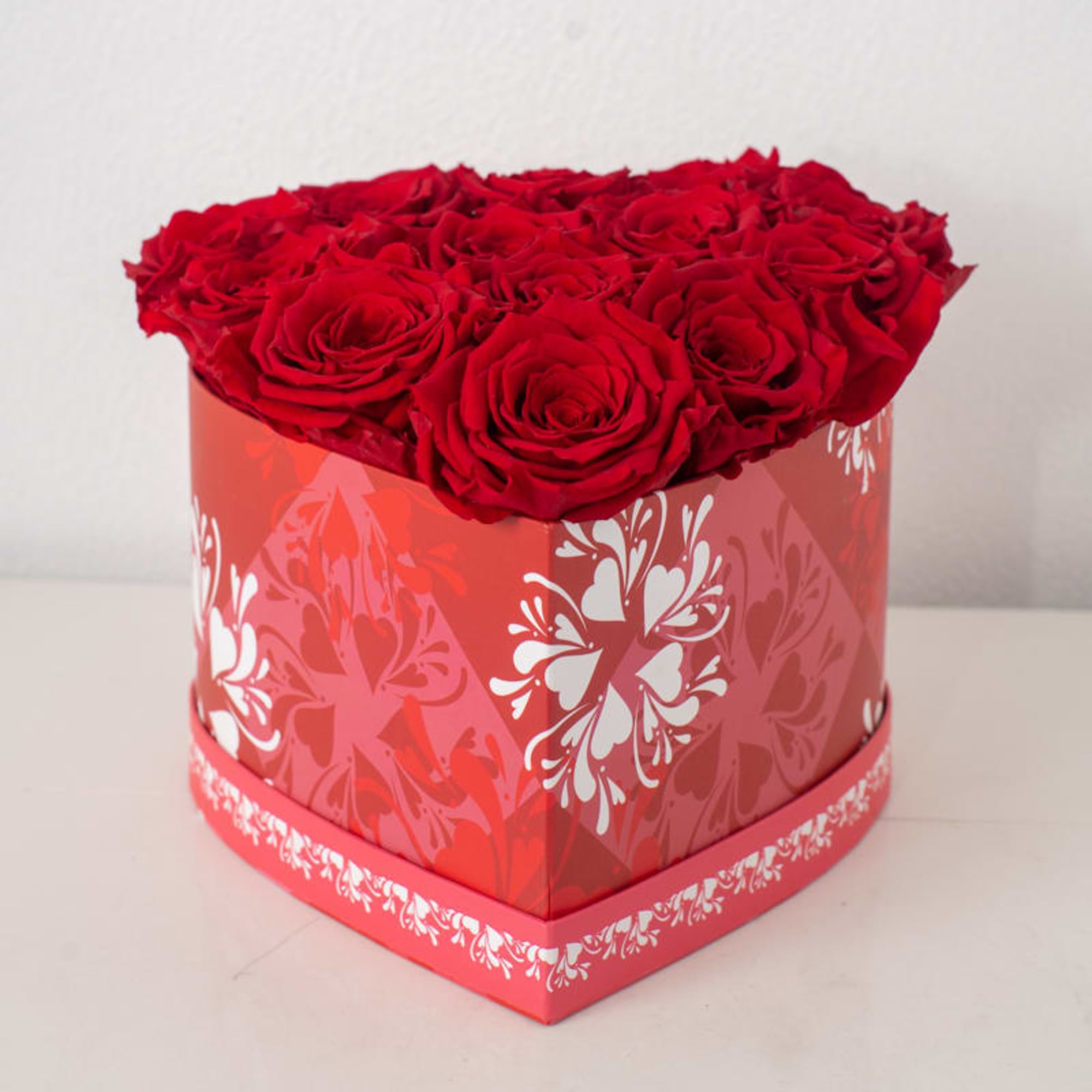 Heart-shaped red box filled with tightly packed red roses on a white surface