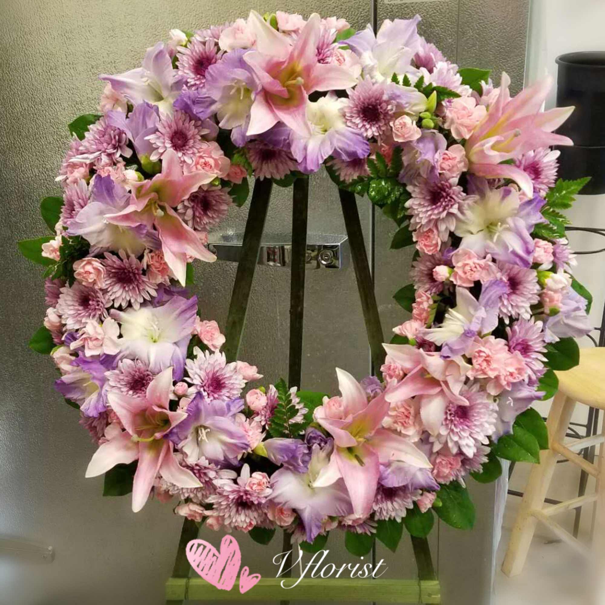 Pink and lavender wreath of lilies, carnations, and mums displayed on a wooden easel