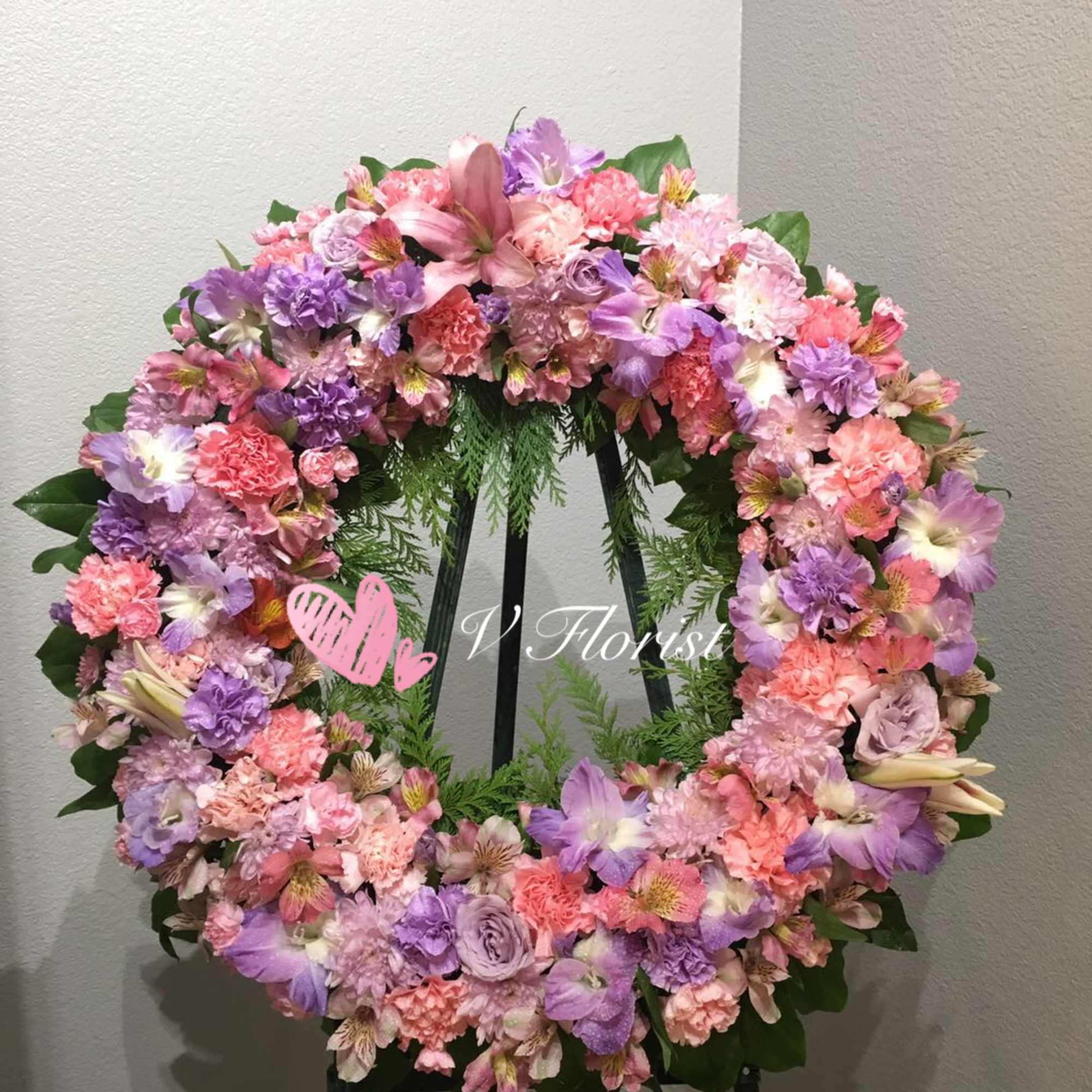 Round standing wreath of pink and lavender flowers on a green easel