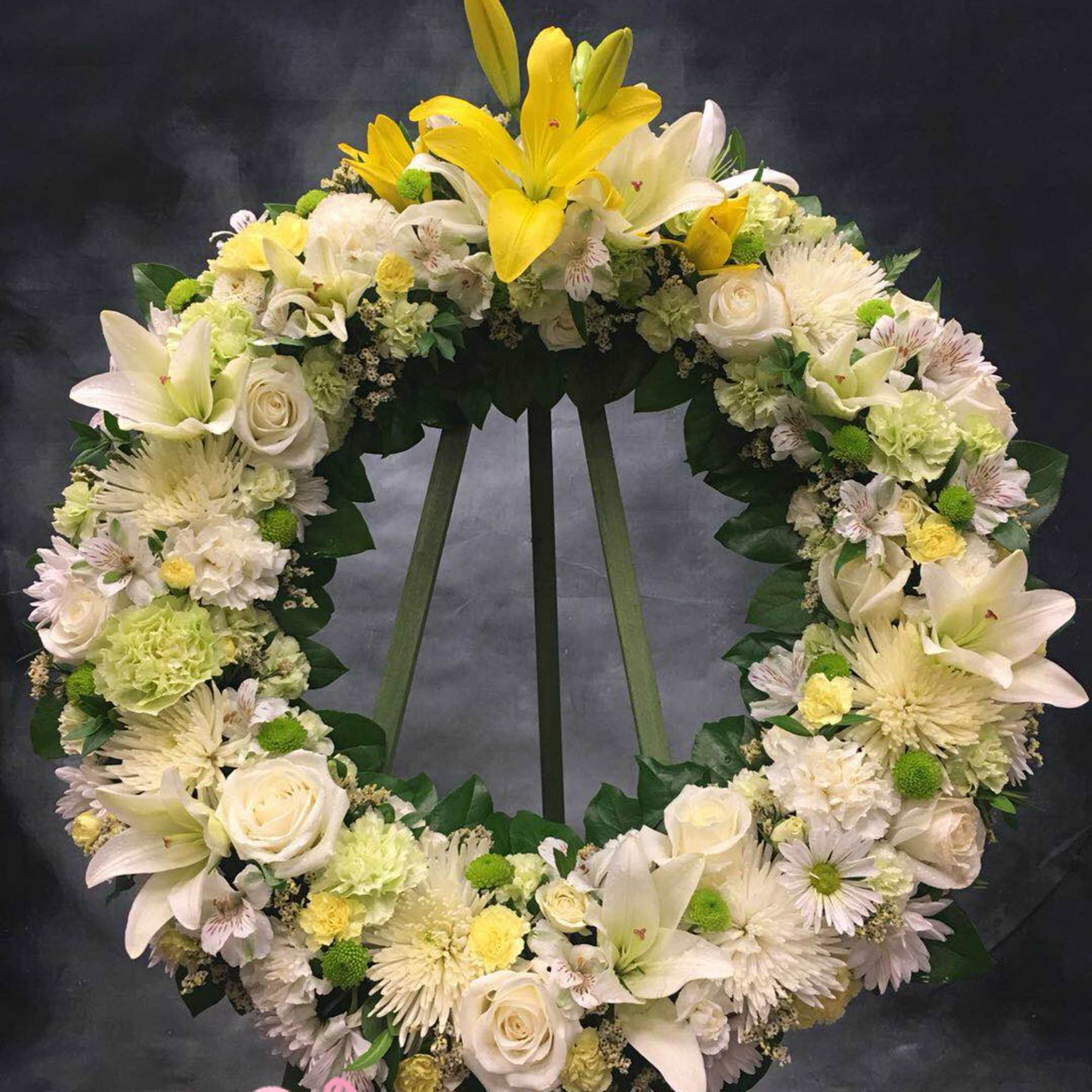 Standing wreath of white and yellow lilies, roses, and mums on a green easel