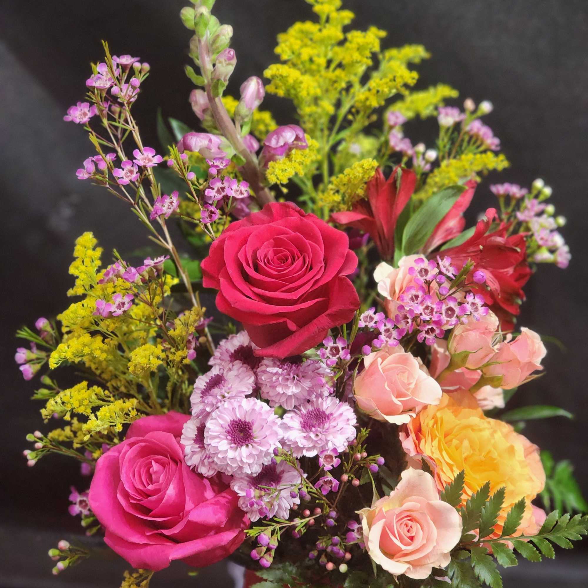 Bright mixed bouquet with pink, peach, and yellow roses and purple mums in a red container