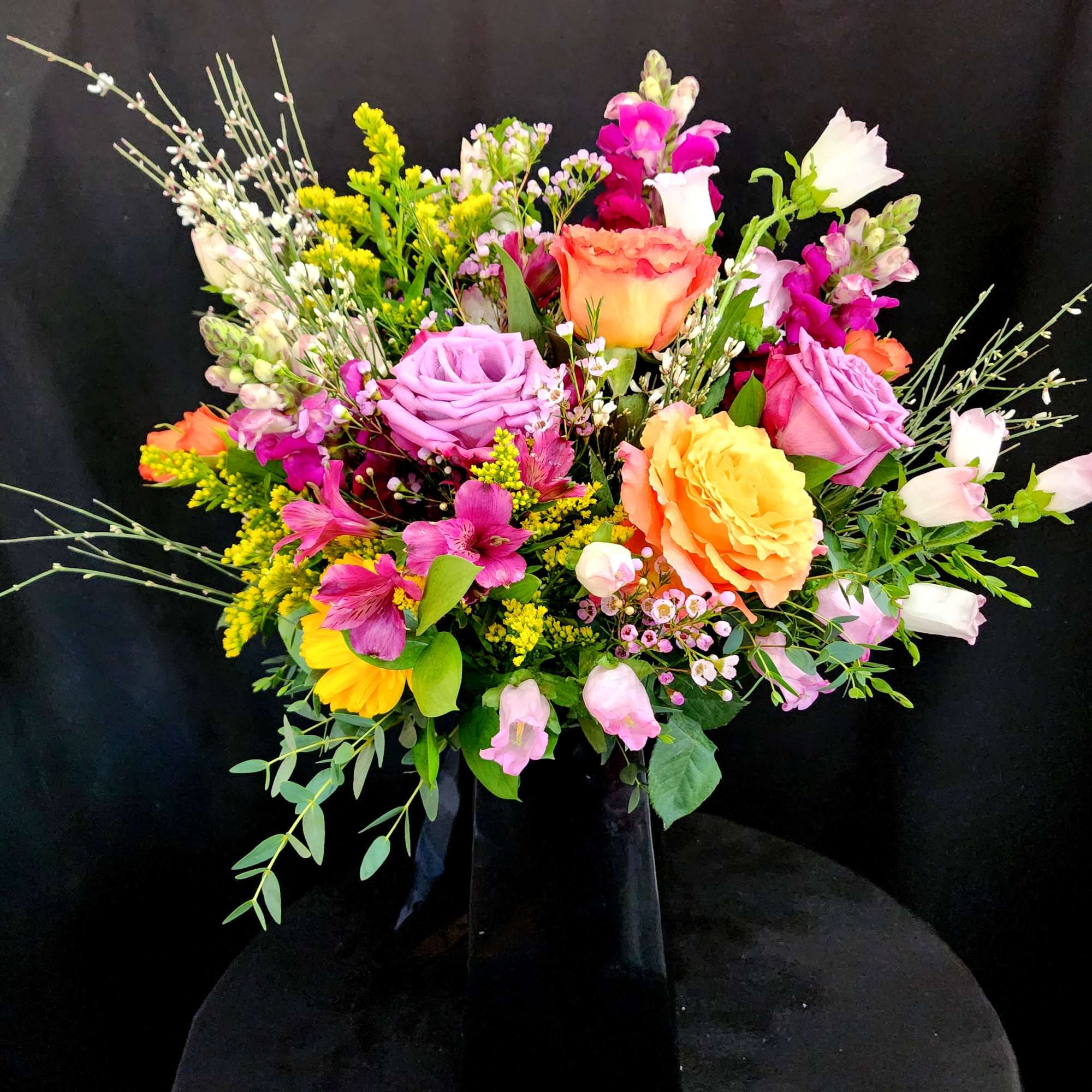 Bright mixed bouquet with pink, purple, and yellow flowers in a tall black vase