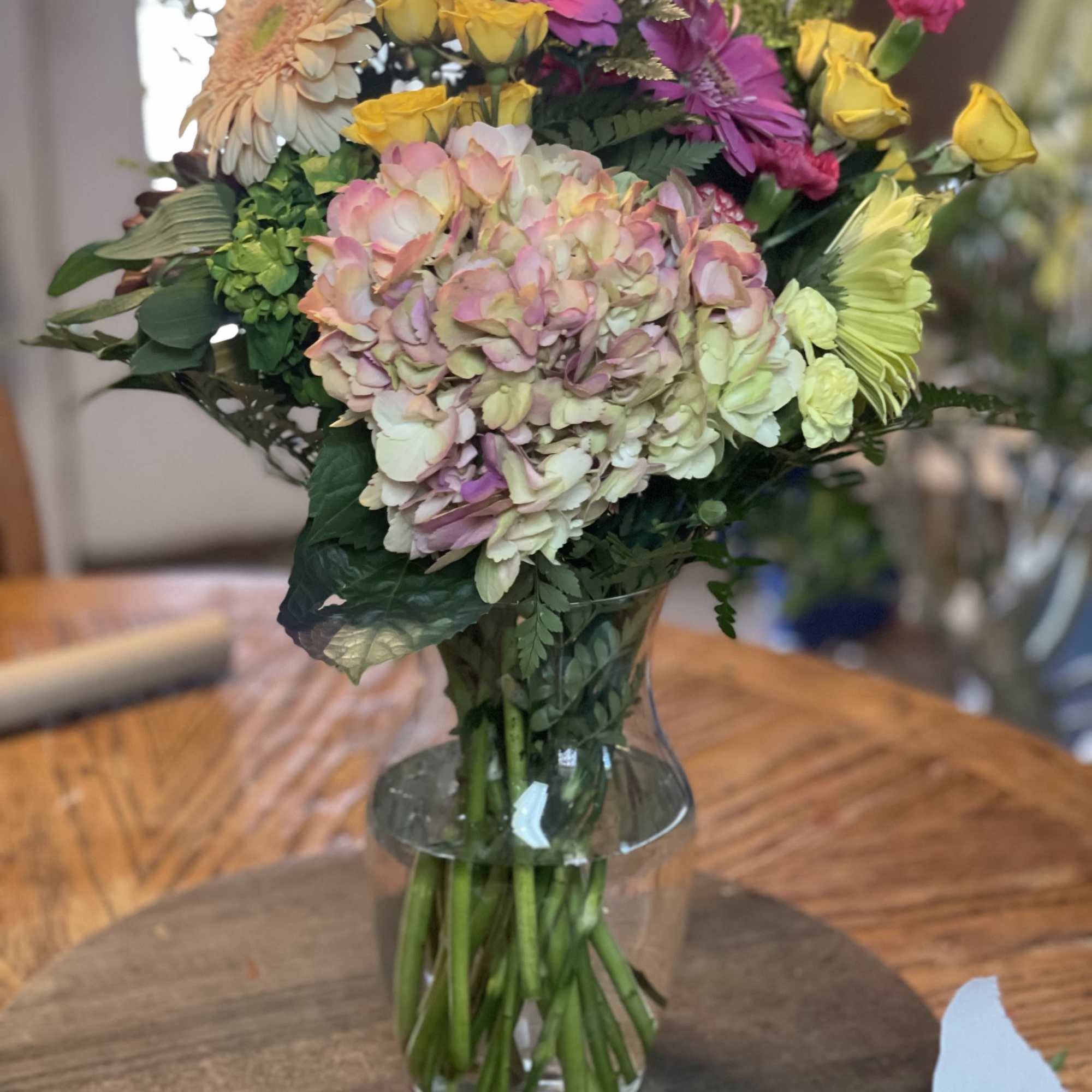 Mixed bouquet with hydrangea, gerbera daisies, and yellow roses in a clear glass vase