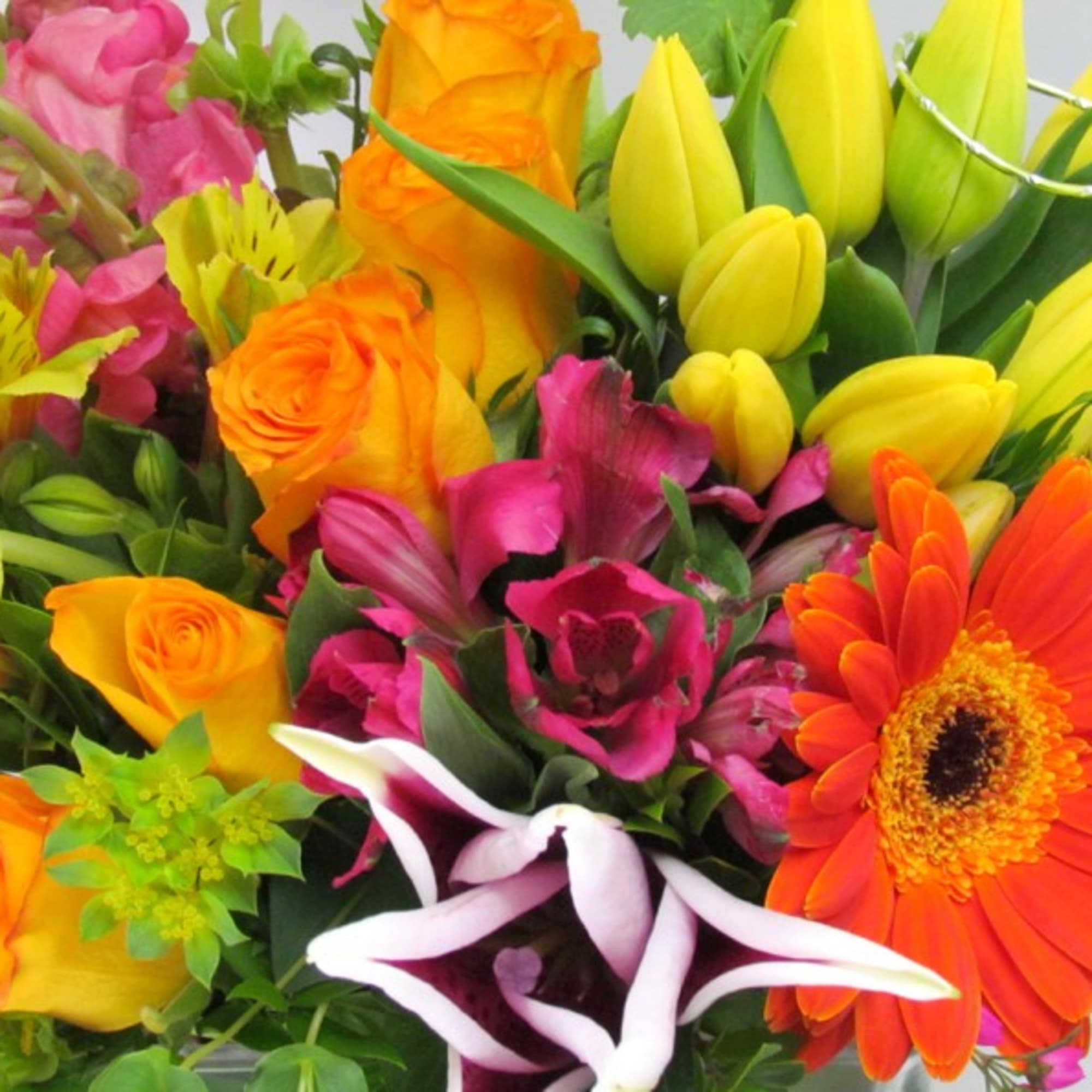 Bright mixed bouquet with orange roses, yellow tulips, pink flowers, and an orange gerbera daisy