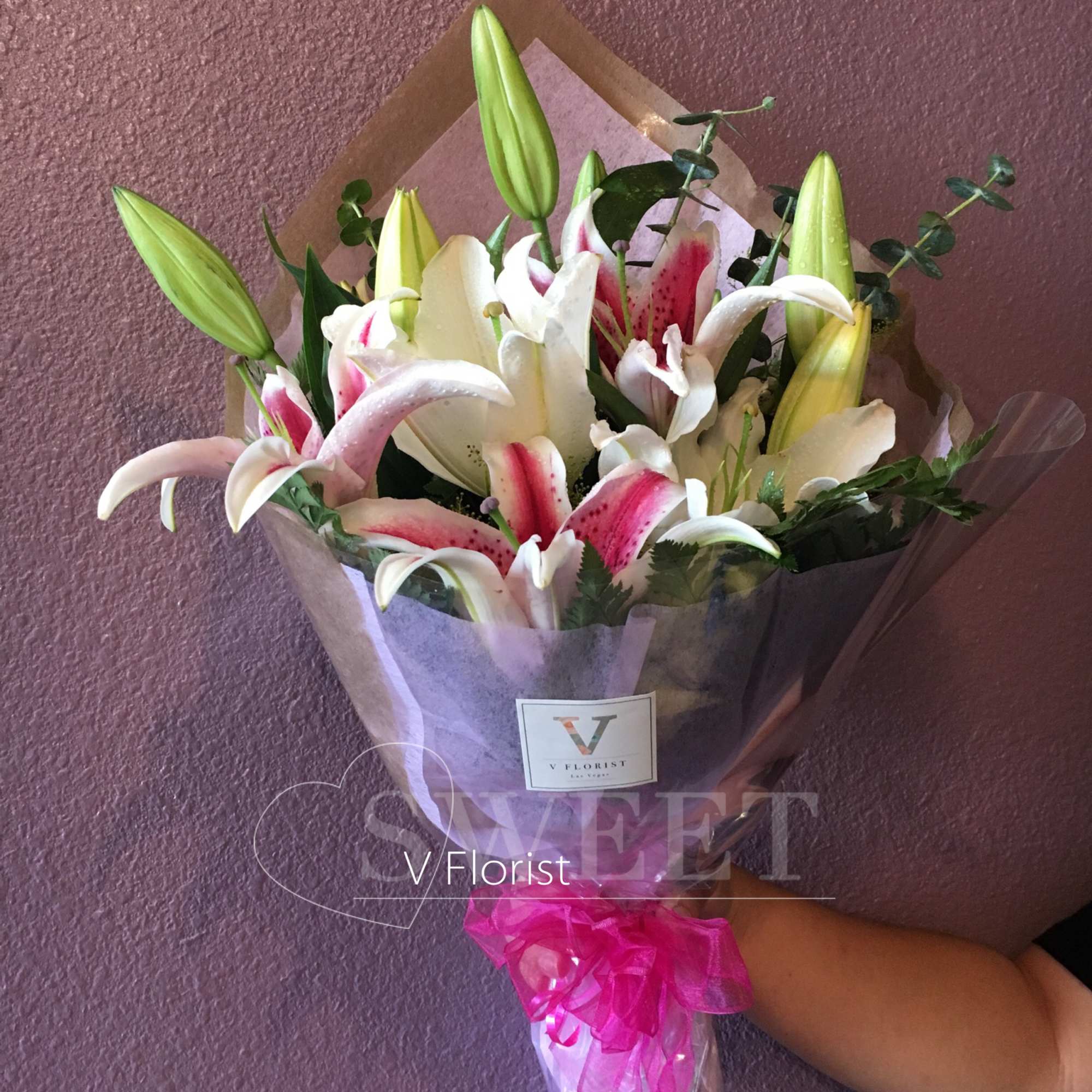Hand-tied bouquet of pink and white lilies with buds, wrapped in clear paper with a bright pink ribbon bow