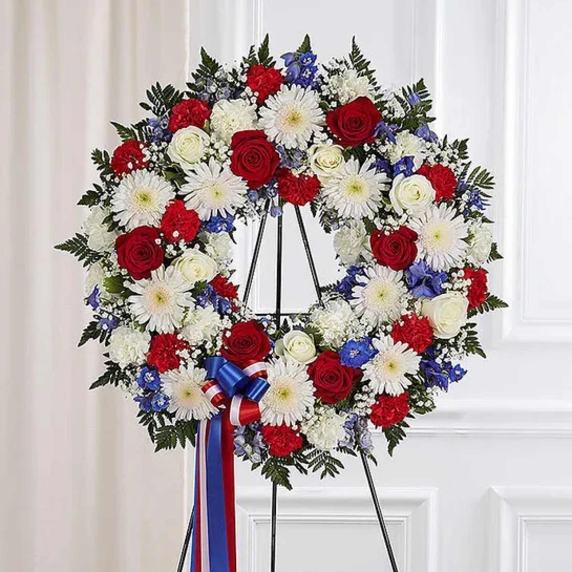 Patriotic red, white, and blue standing wreath with roses, carnations, and daisies on a metal easel
