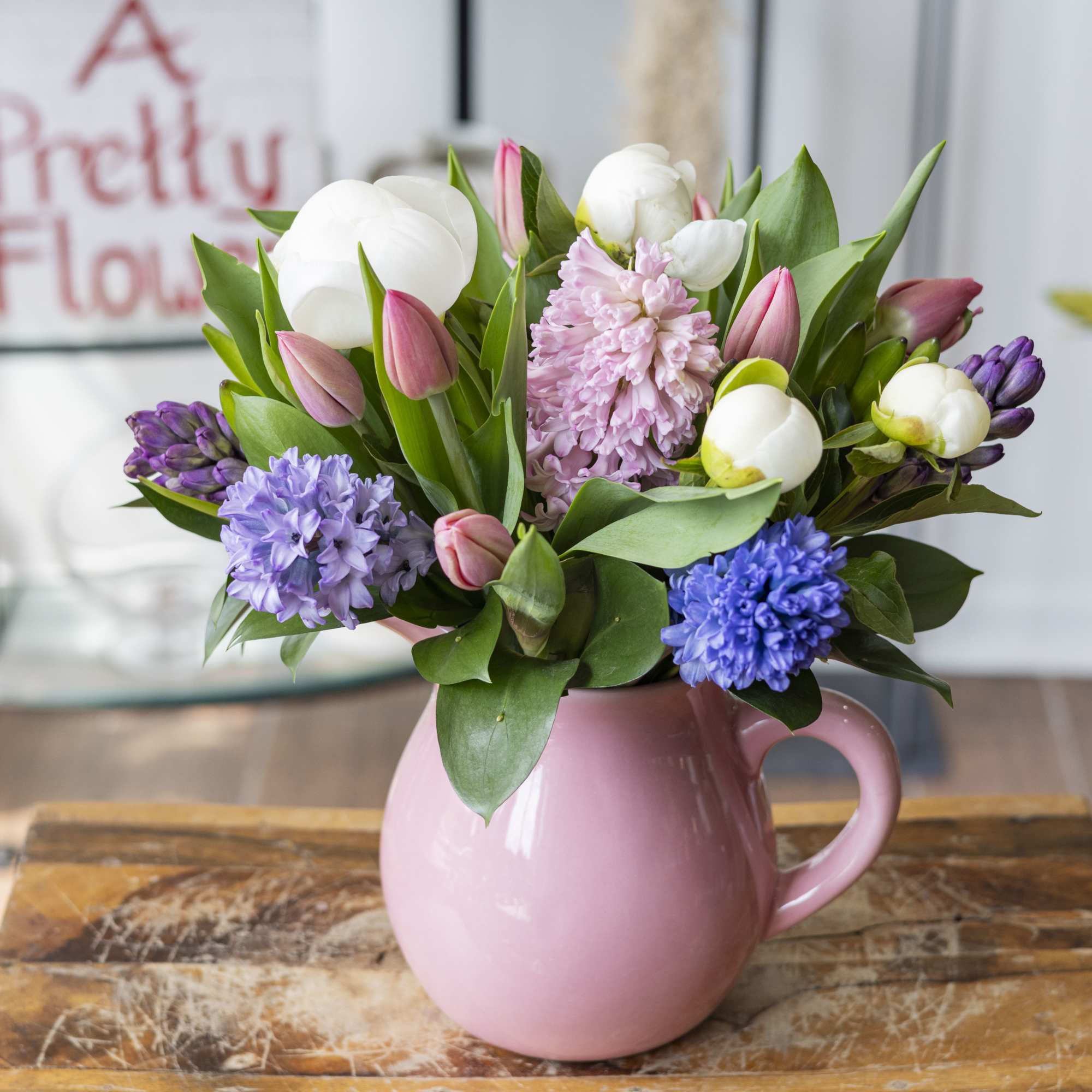 Mixed pink tulips, white blooms, and purple hyacinths in a pink ceramic pitcher