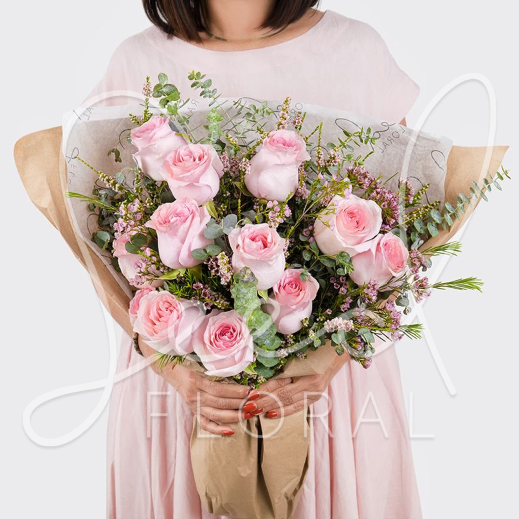 Hand-tied bouquet of light pink roses with small pink filler flowers wrapped in kraft and tissue paper