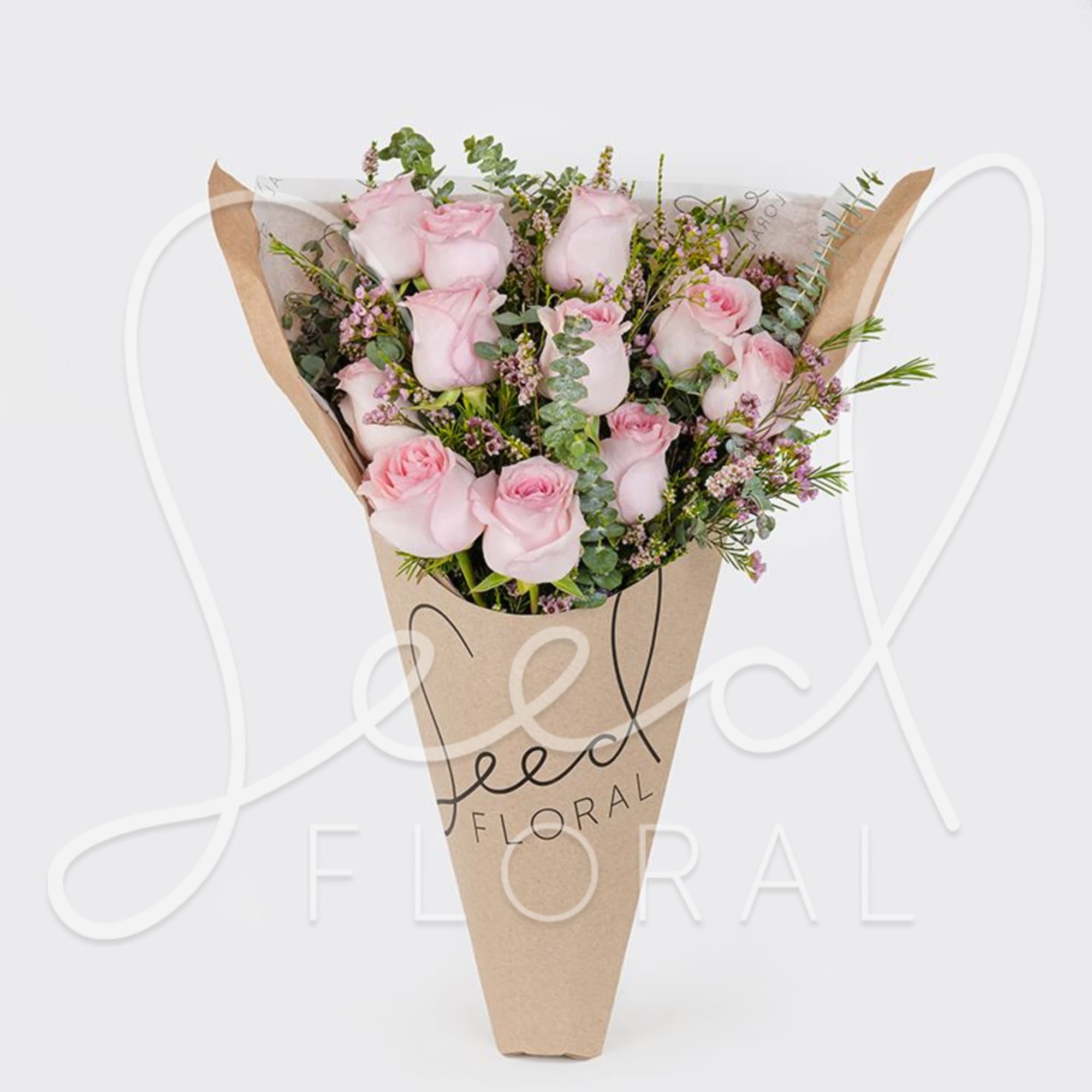 Bouquet of light pink roses with filler flowers wrapped in a kraft paper cone.