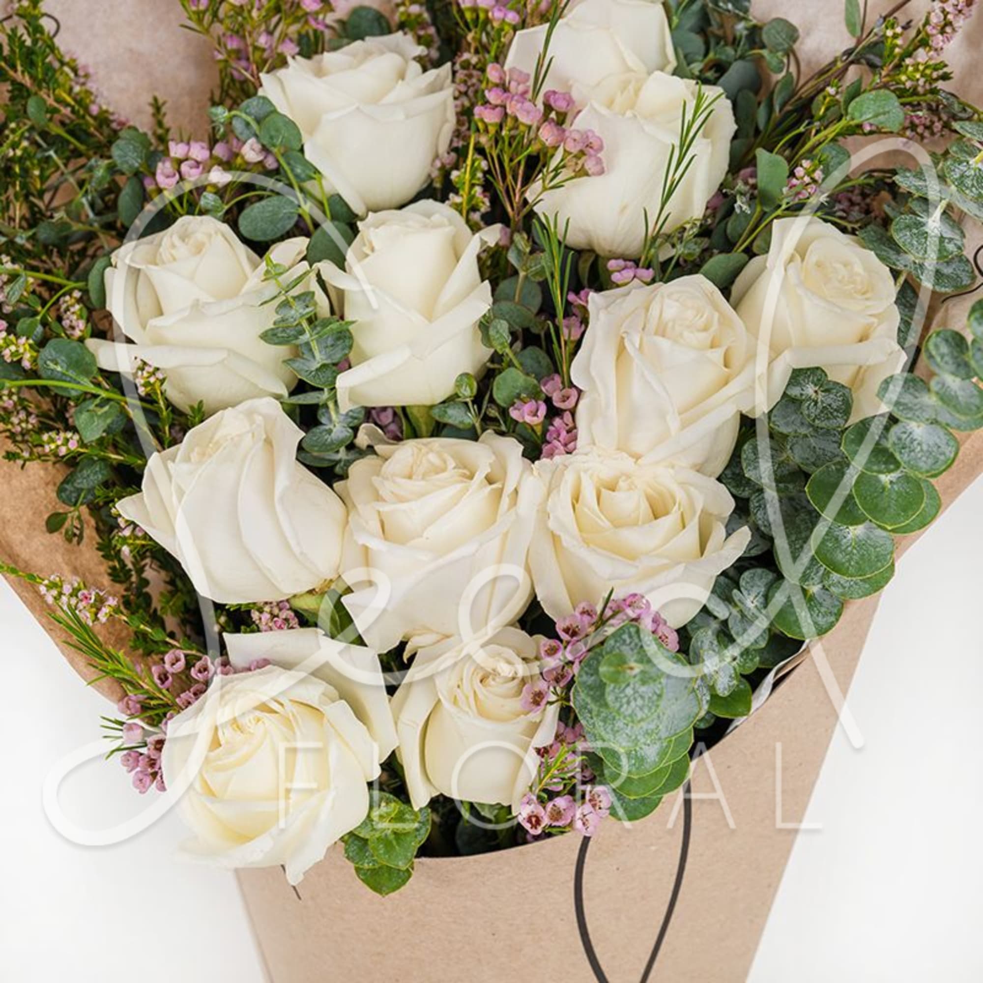 Hand-tied bouquet of white roses with small pink blossoms wrapped in brown paper.
