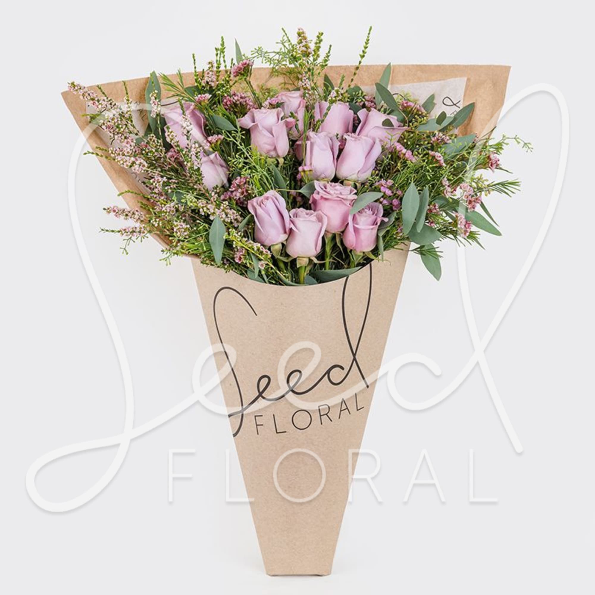 Cone-wrapped bouquet of lavender roses with tiny pink filler flowers in kraft paper.