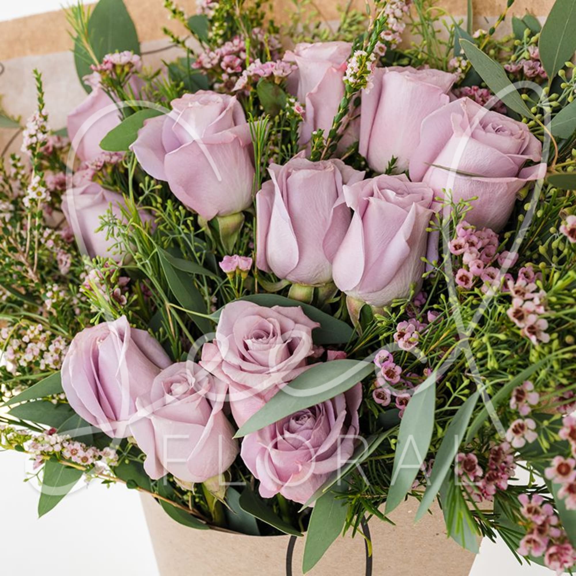 Arrangement of lavender roses with tiny pink filler flowers in a kraft paper bag-style container