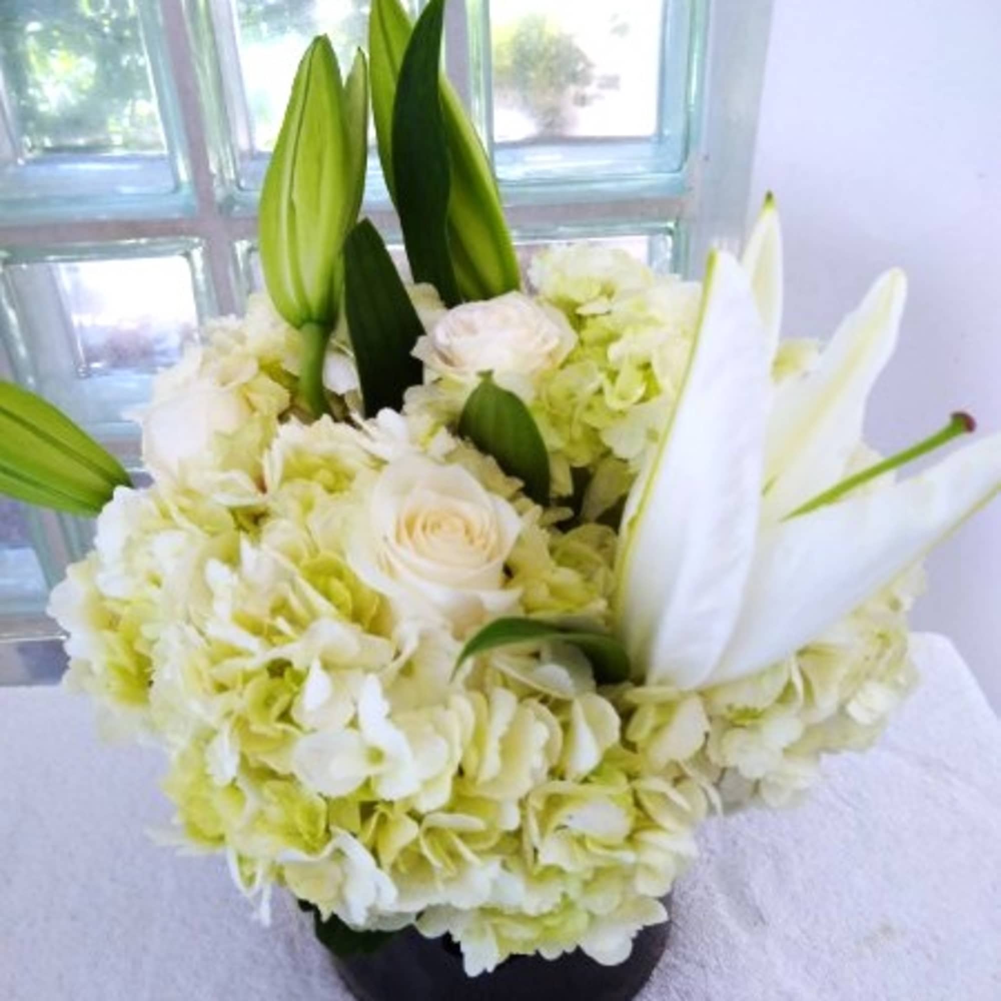 Round arrangement of white hydrangeas, roses, and lilies in a black vase