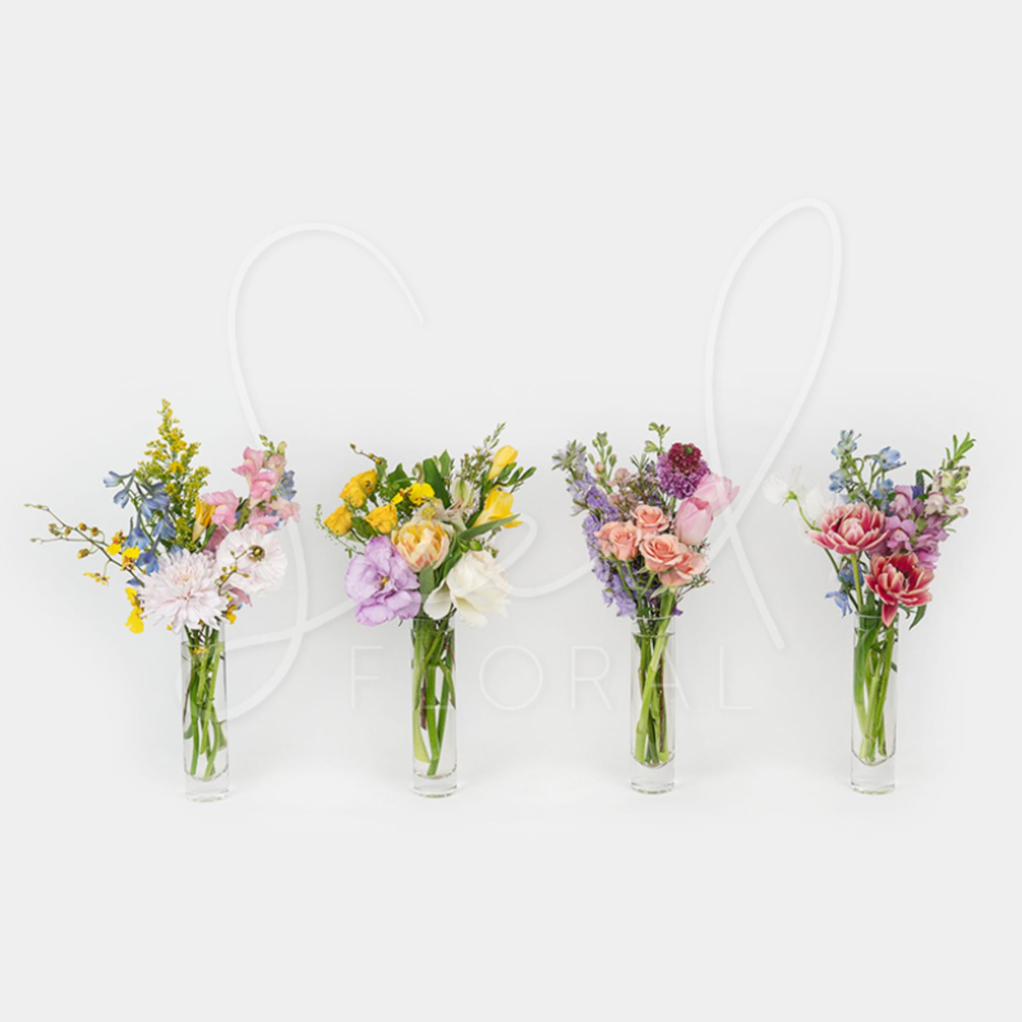 Four small mixed spring flower arrangements in tall clear glass bud vases in a row.