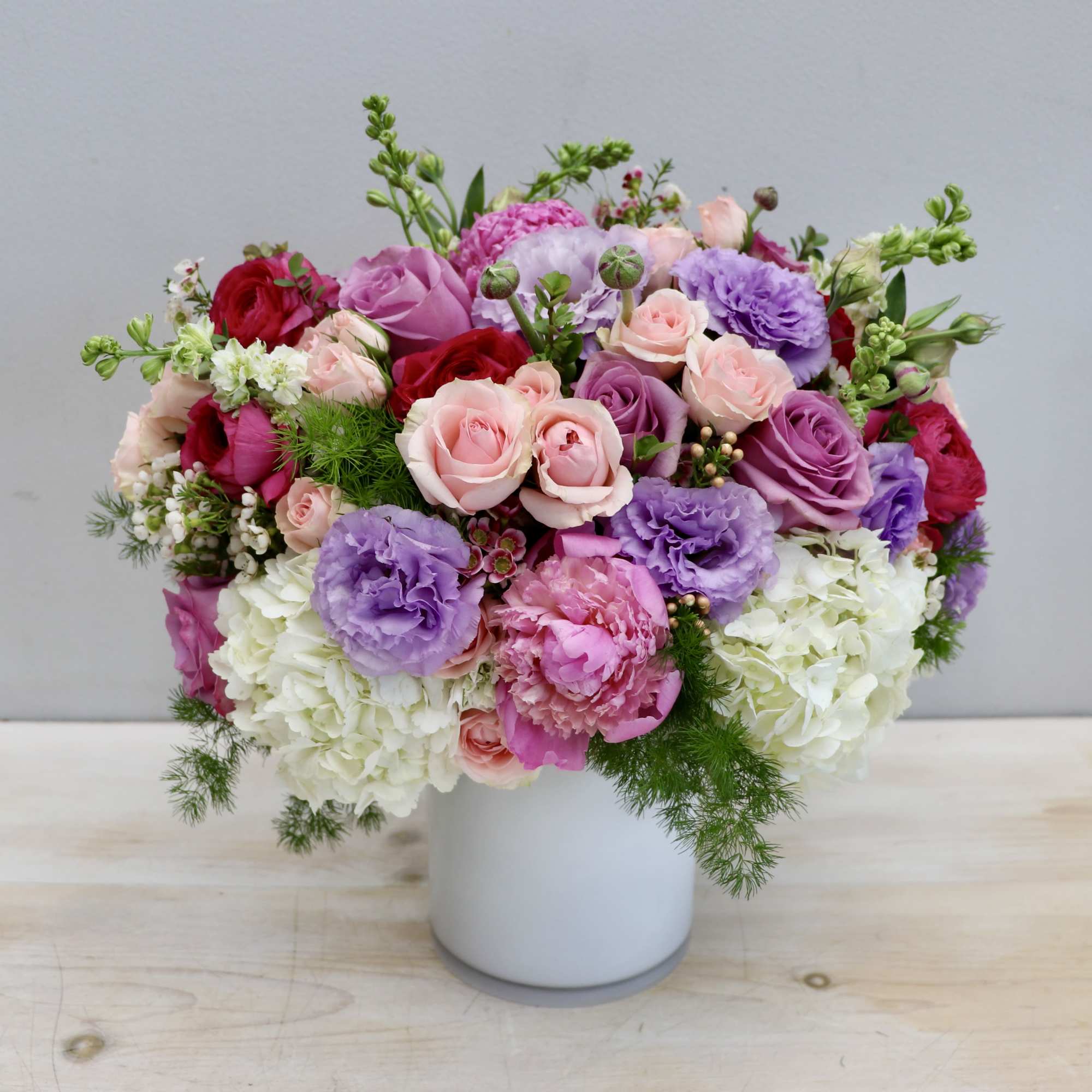 Low arrangement of pink, purple, red, and white flowers in a white cylinder vase