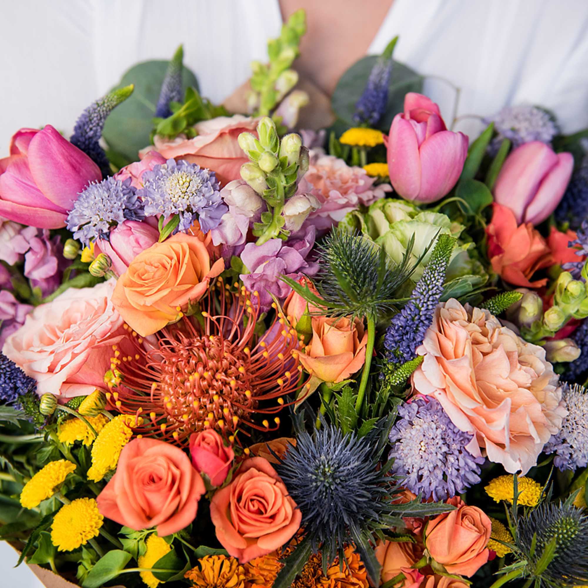 Lush hand-tied bouquet of pink tulips, peach roses, and assorted colorful blooms