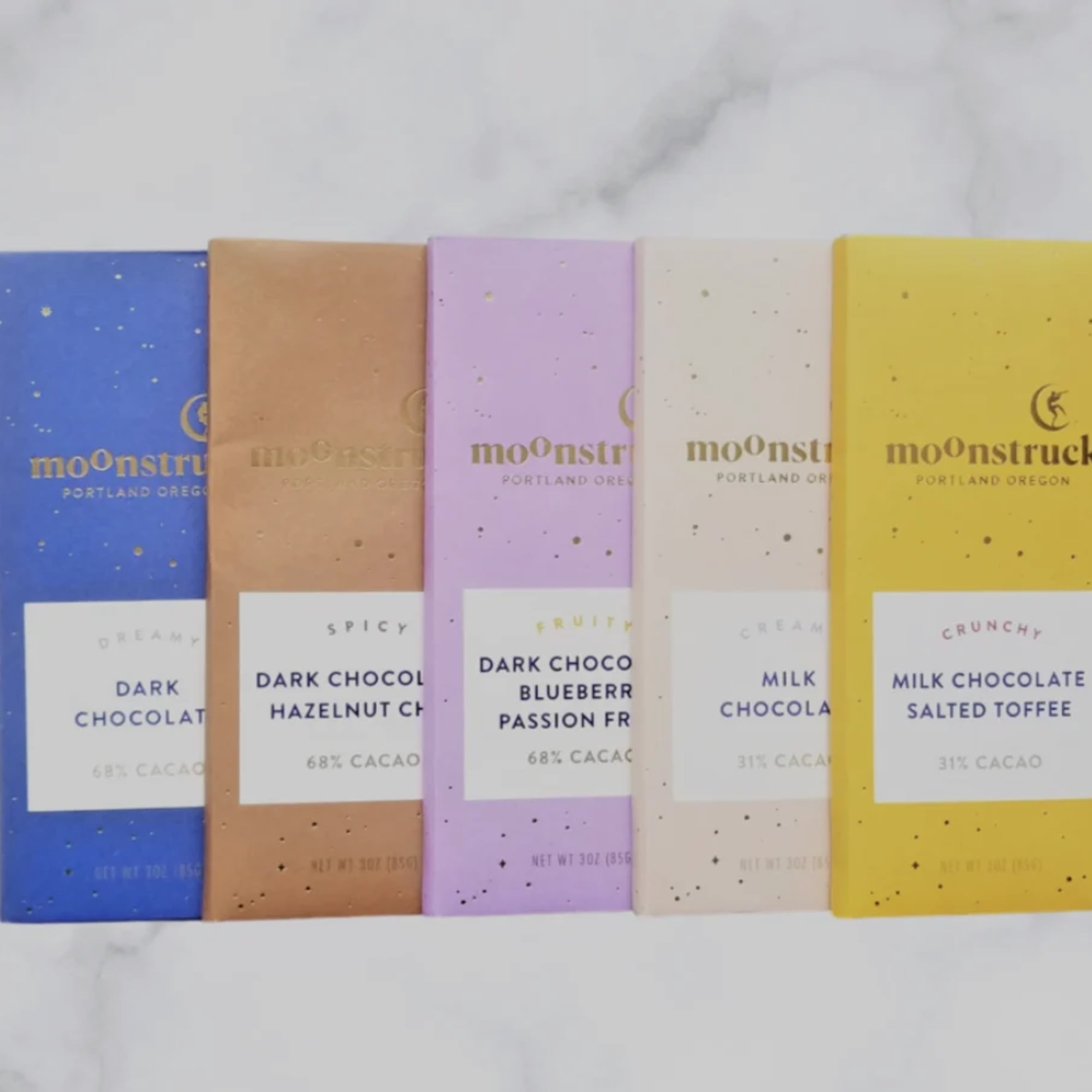 Row of five assorted Moonstruck chocolate bars in colorful wrappers on a marble surface