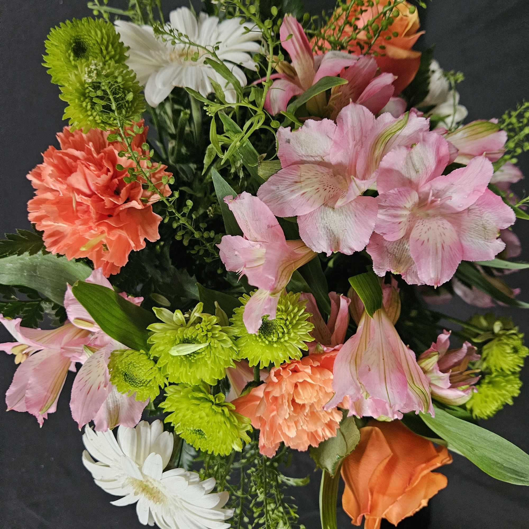 Mixed bouquet of pink alstroemeria, orange carnations and rose, green mums, and white daisies.