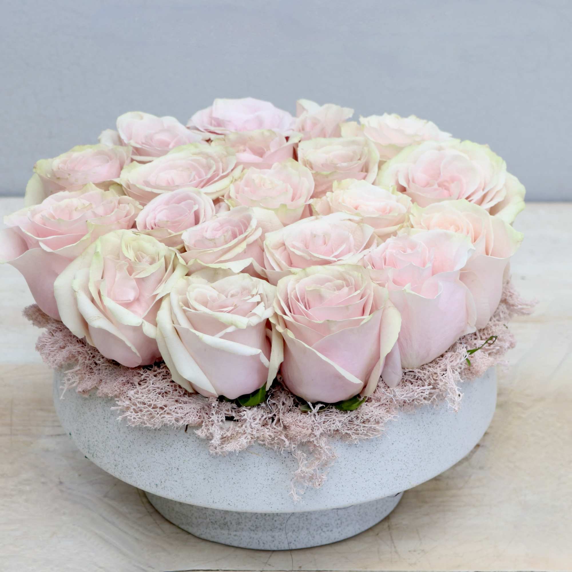 Low round arrangement of pale pink roses tightly packed in a white ceramic bowl.
