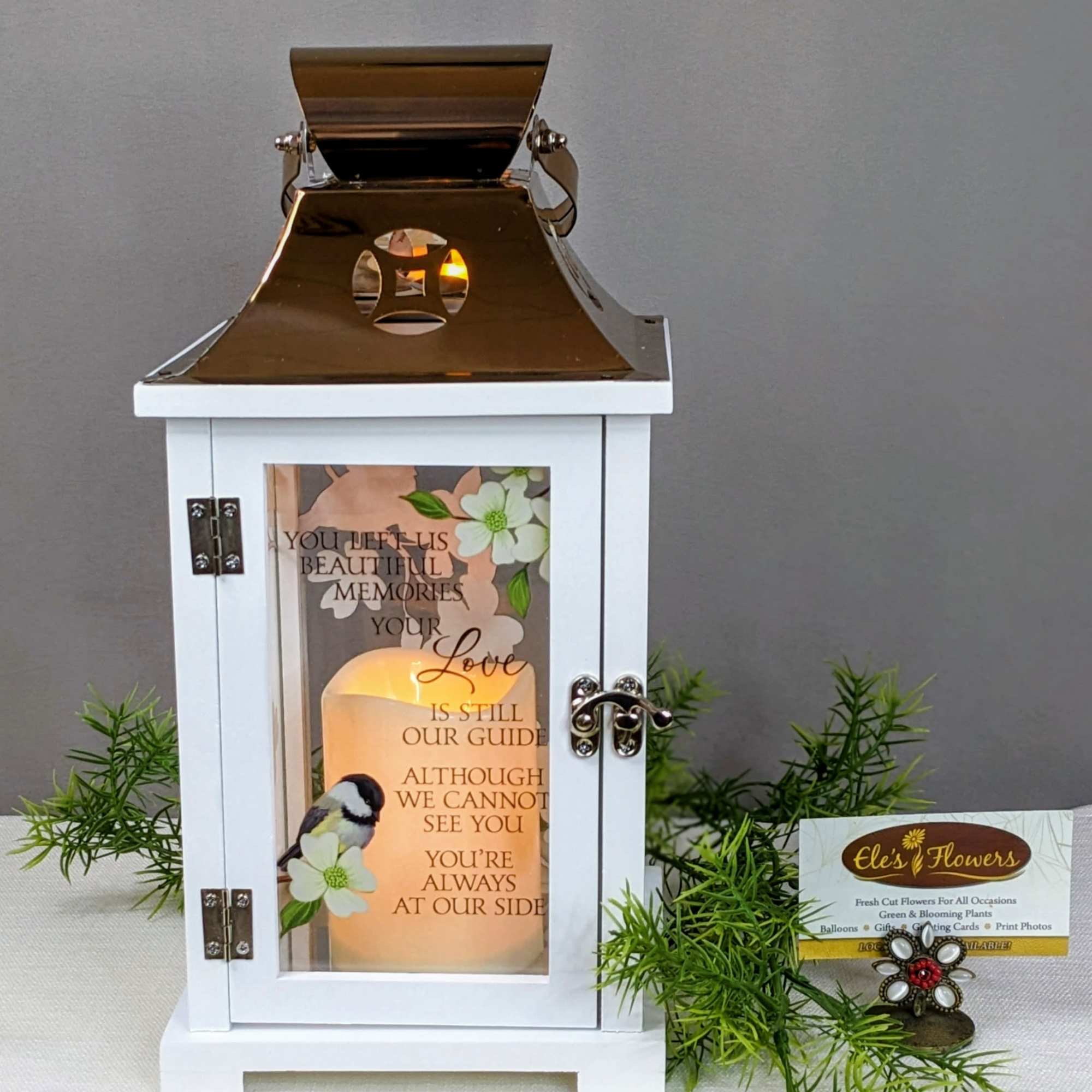 White memorial lantern with gold top and glowing candle, printed with verse and bird illustration.