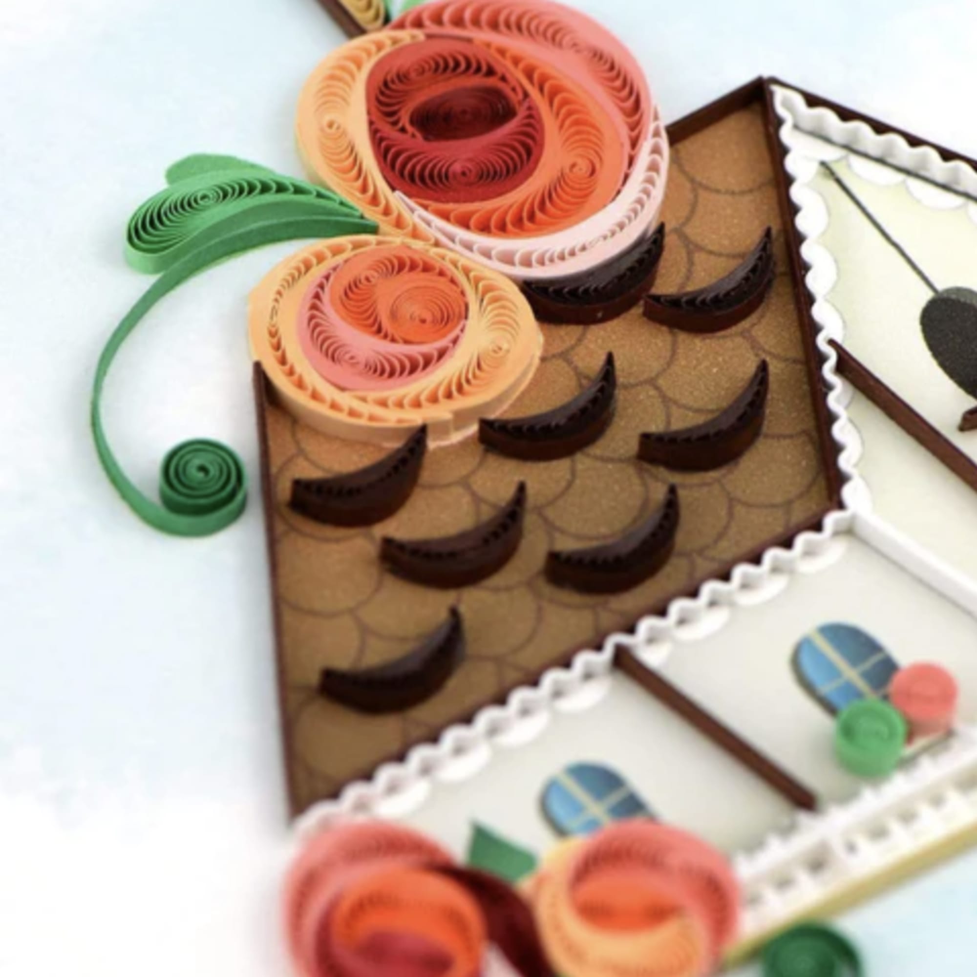 Paper quilled design of a house roof with curled orange and peach flowers and green scroll accents