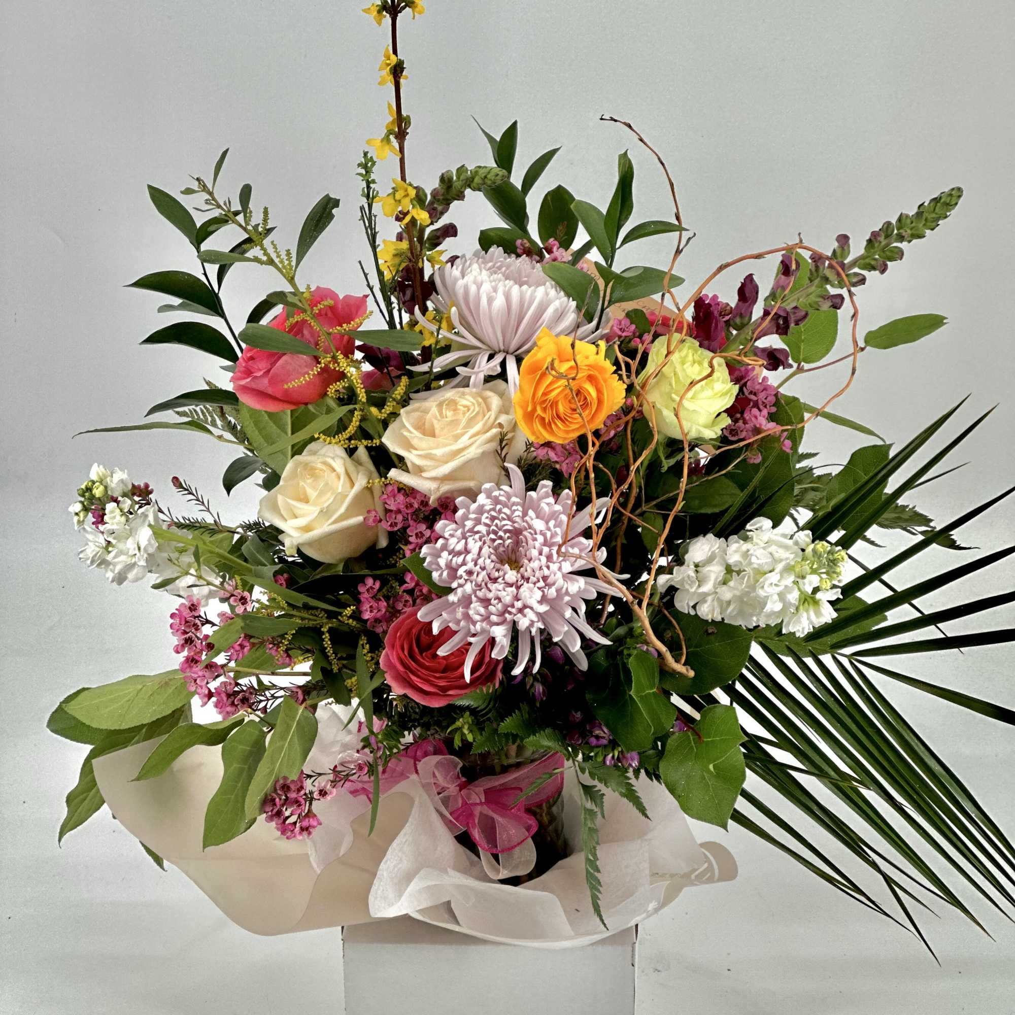 Tall mixed arrangement of pink, white, and yellow flowers with greenery in a white box base