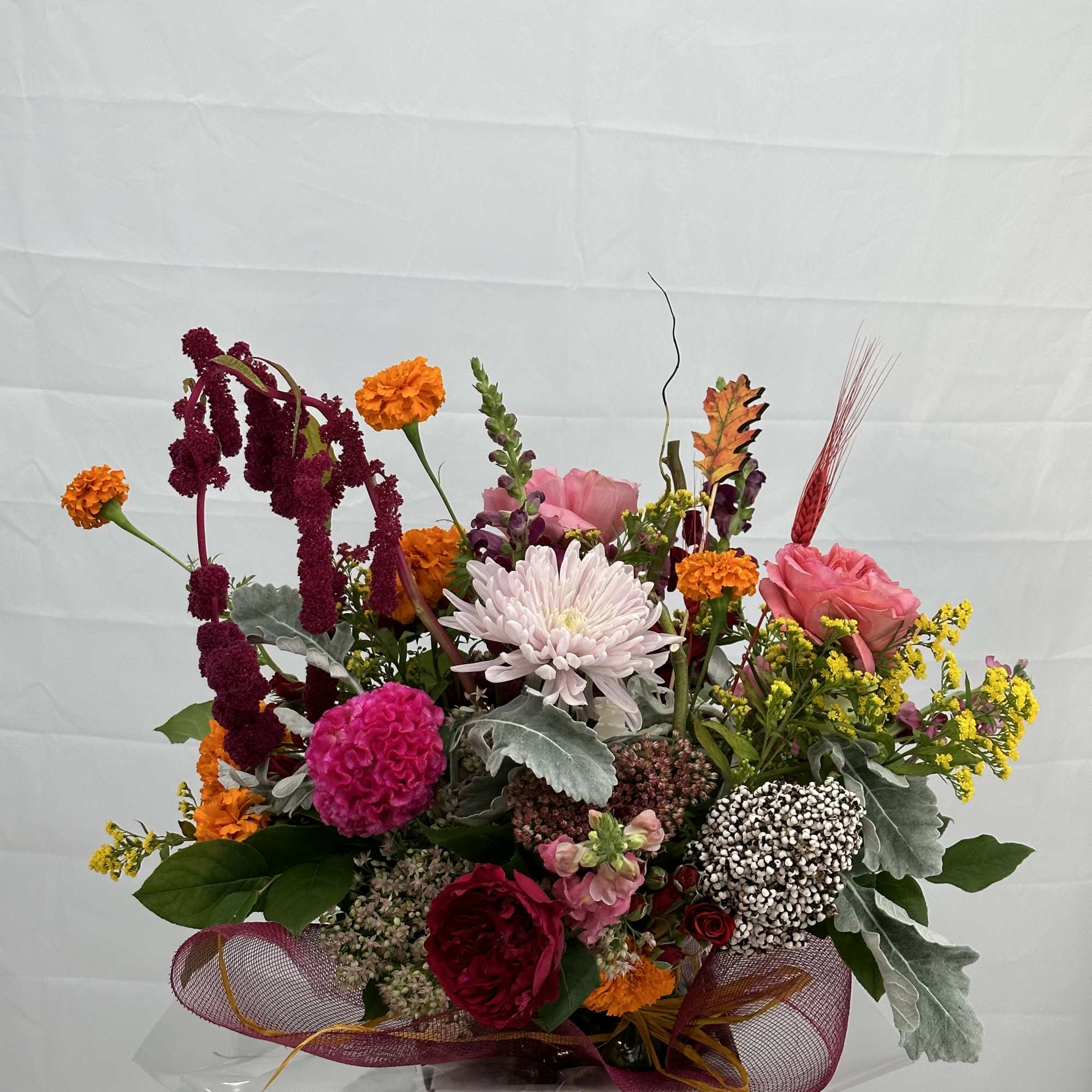 Colorful arrangement with pink roses, marigolds, and mums in a white box with mesh ribbon