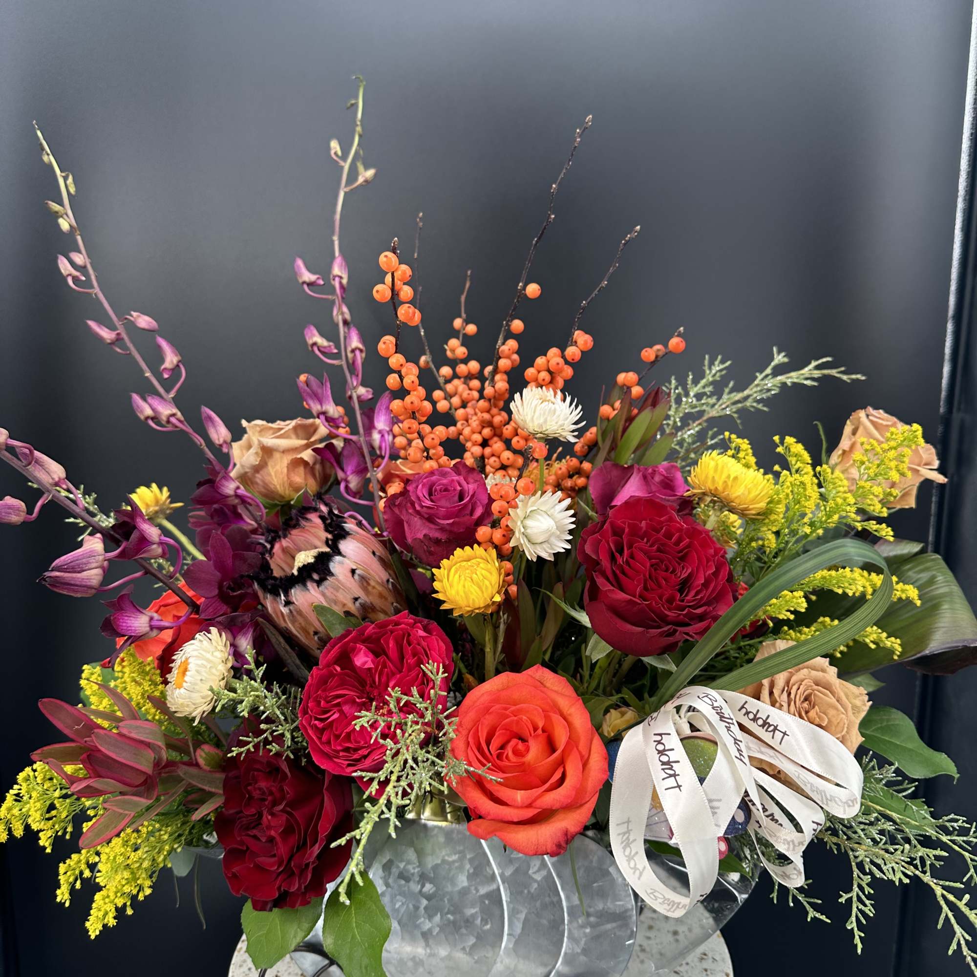 Vibrant arrangement of red and orange flowers with berries in a metal wagon container.