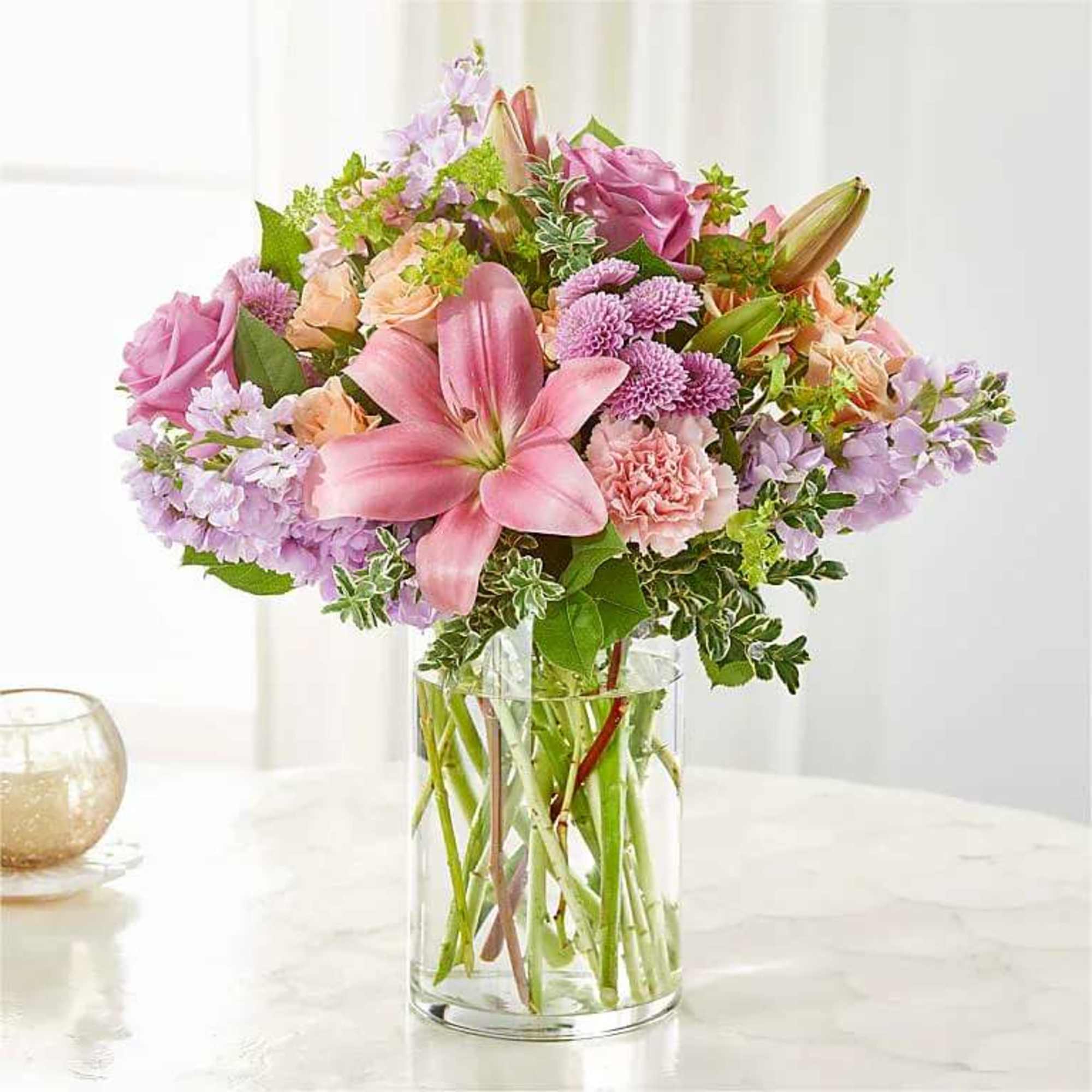 Mixed bouquet of pink lilies, roses, carnations, and lavender flowers in a clear glass vase