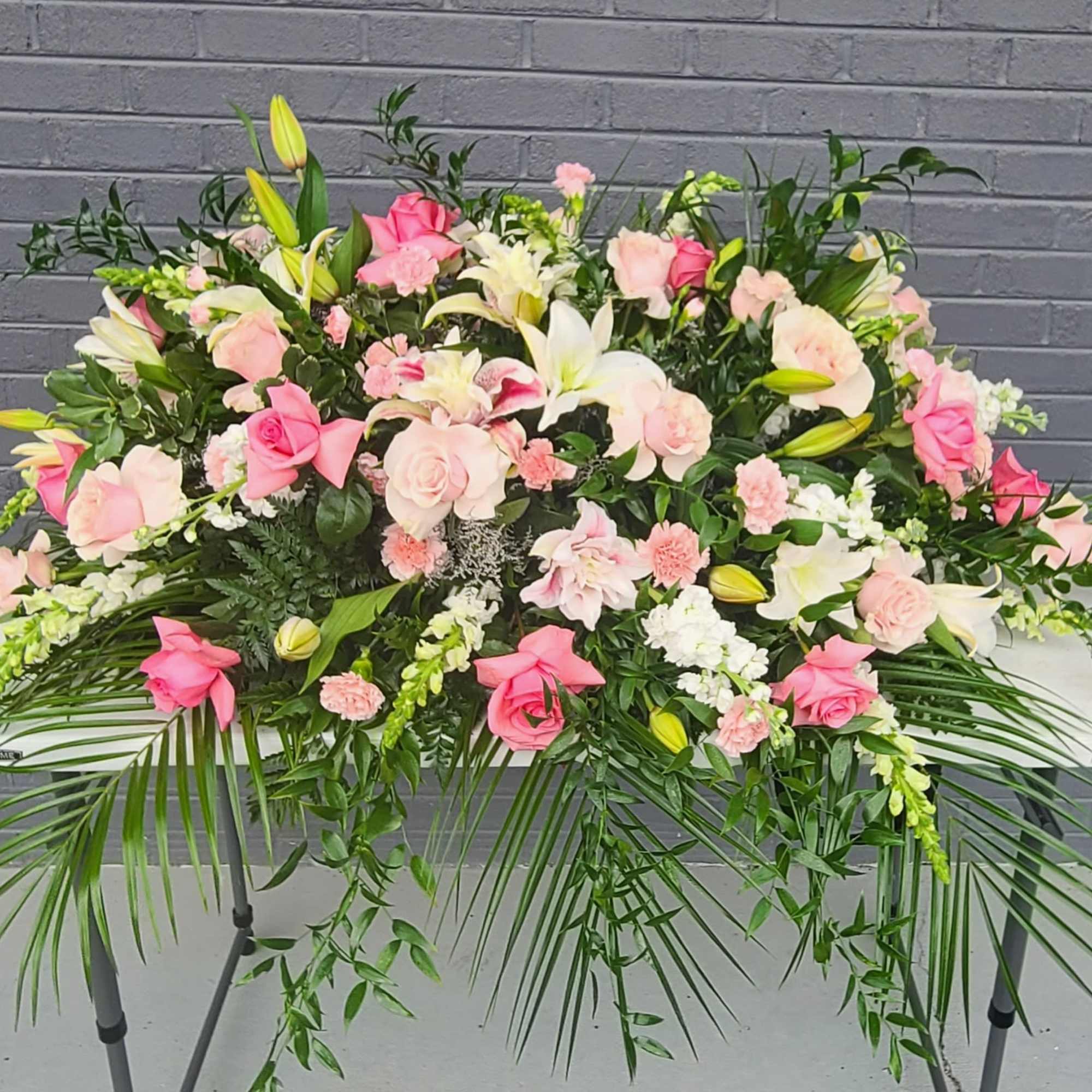 Soft blush roses and creamy white lilies form a tender, elongated casket